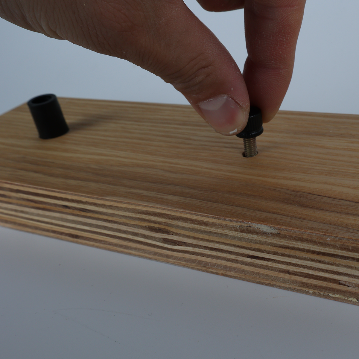 Una mano atornillando una clavija negra en una superficie de madera clara, con otra clavija ya colocada.