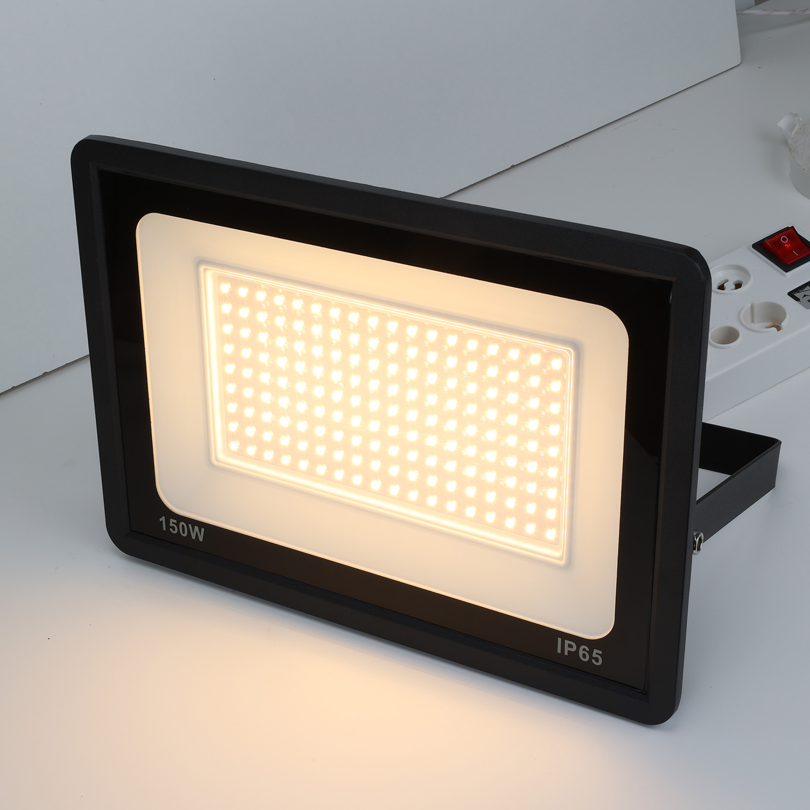Un foco negro con luz blanca sobre una superficie blanca. La luz está encendida. Etiqueta IP65.