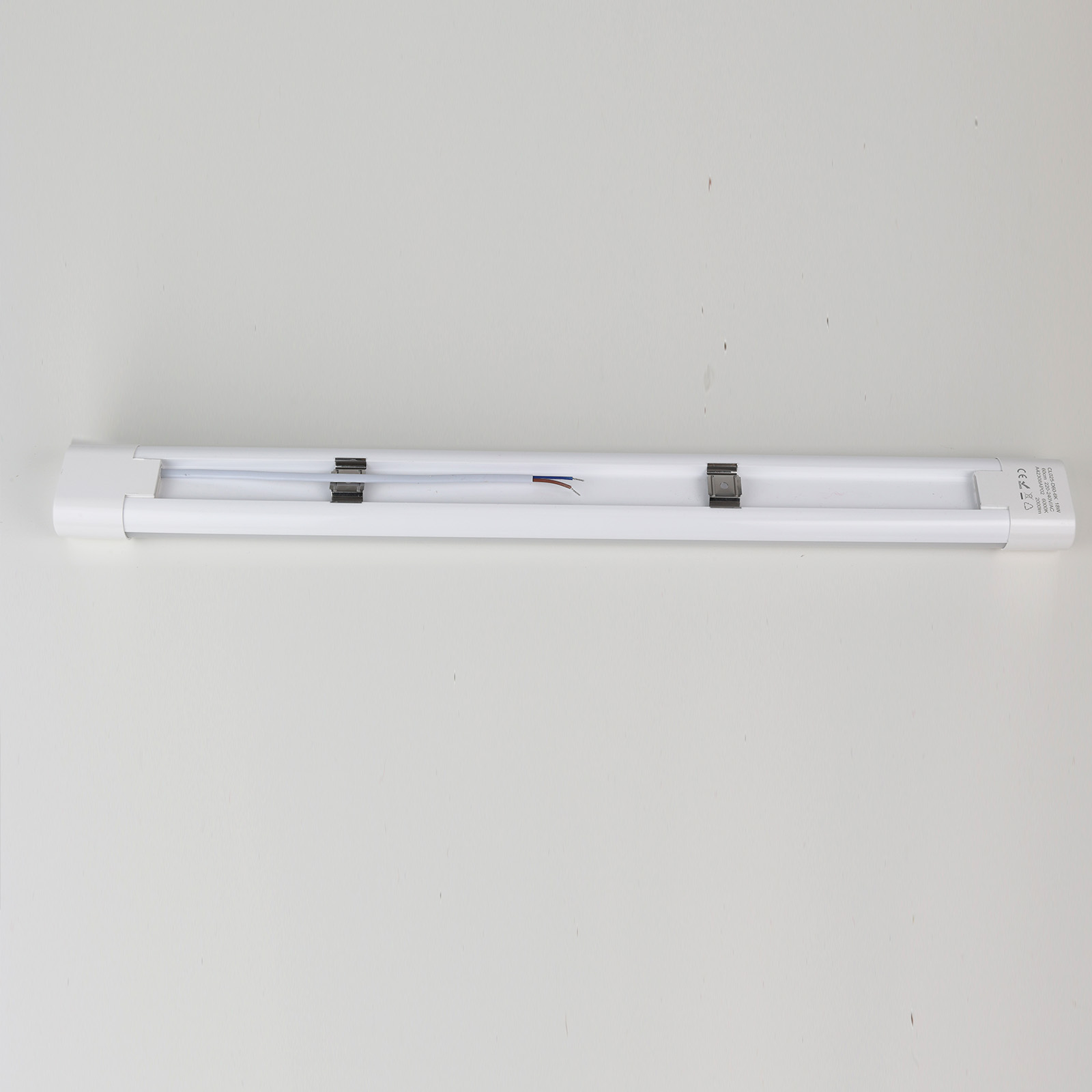 Luminaria LED blanca, larga y delgada, con cableado interno visible, sobre blanco.