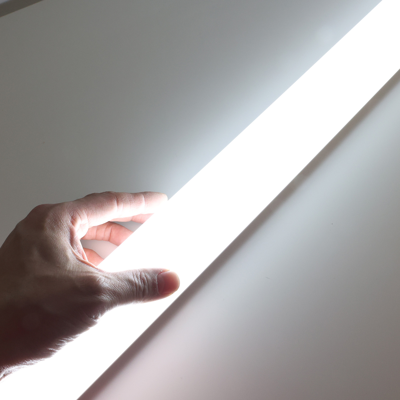 Una mano toca una barra de luz blanca brillante. El fondo es blanco.