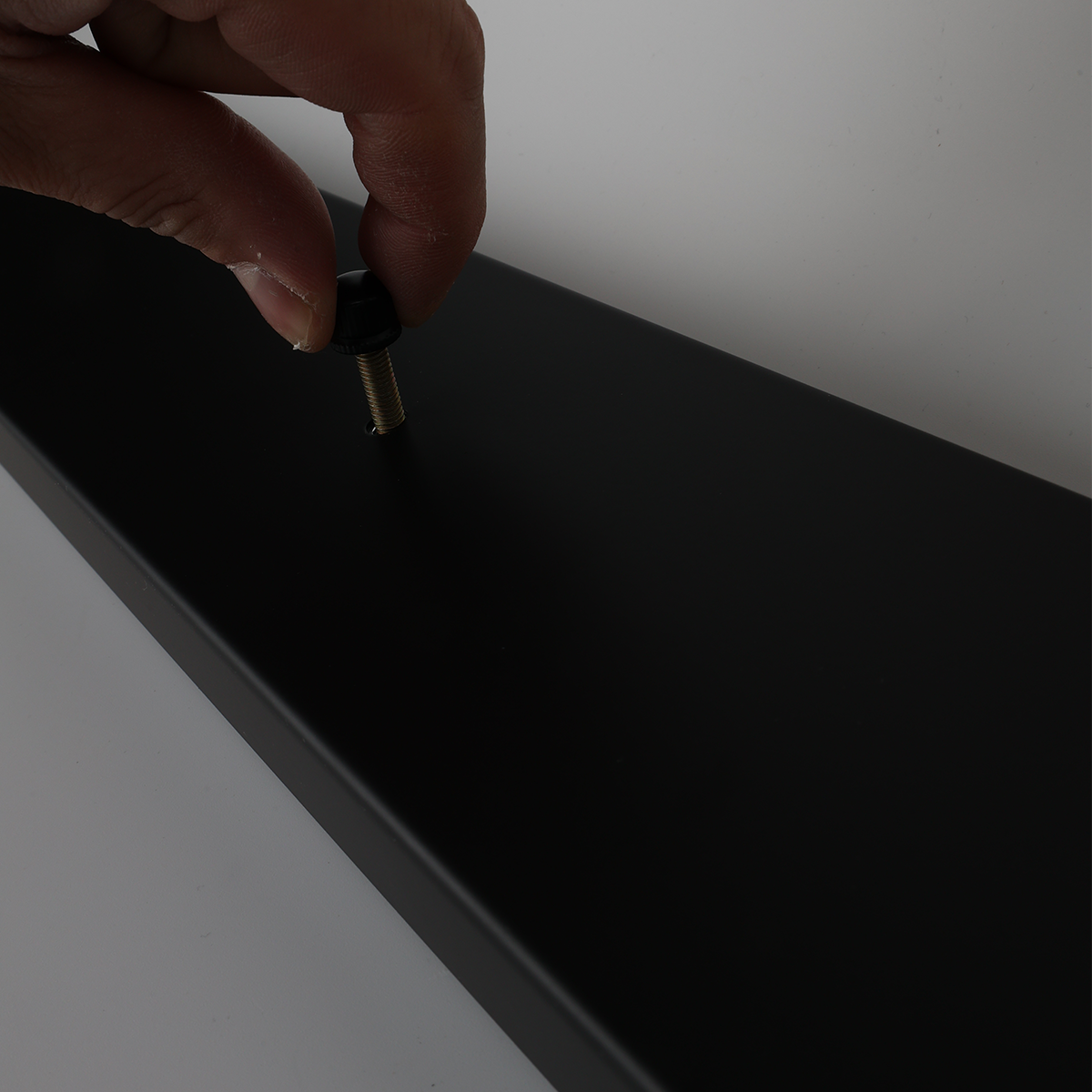 Una mano atornillando un tornillo negro en un soporte rectangular negro.