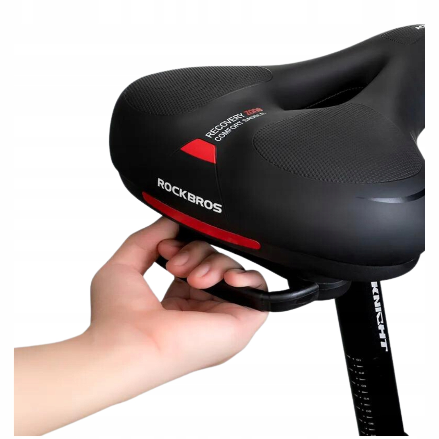 Ręka trzyma czarne siodełko rowerowe. Siodło jest na czarnej sztycy.