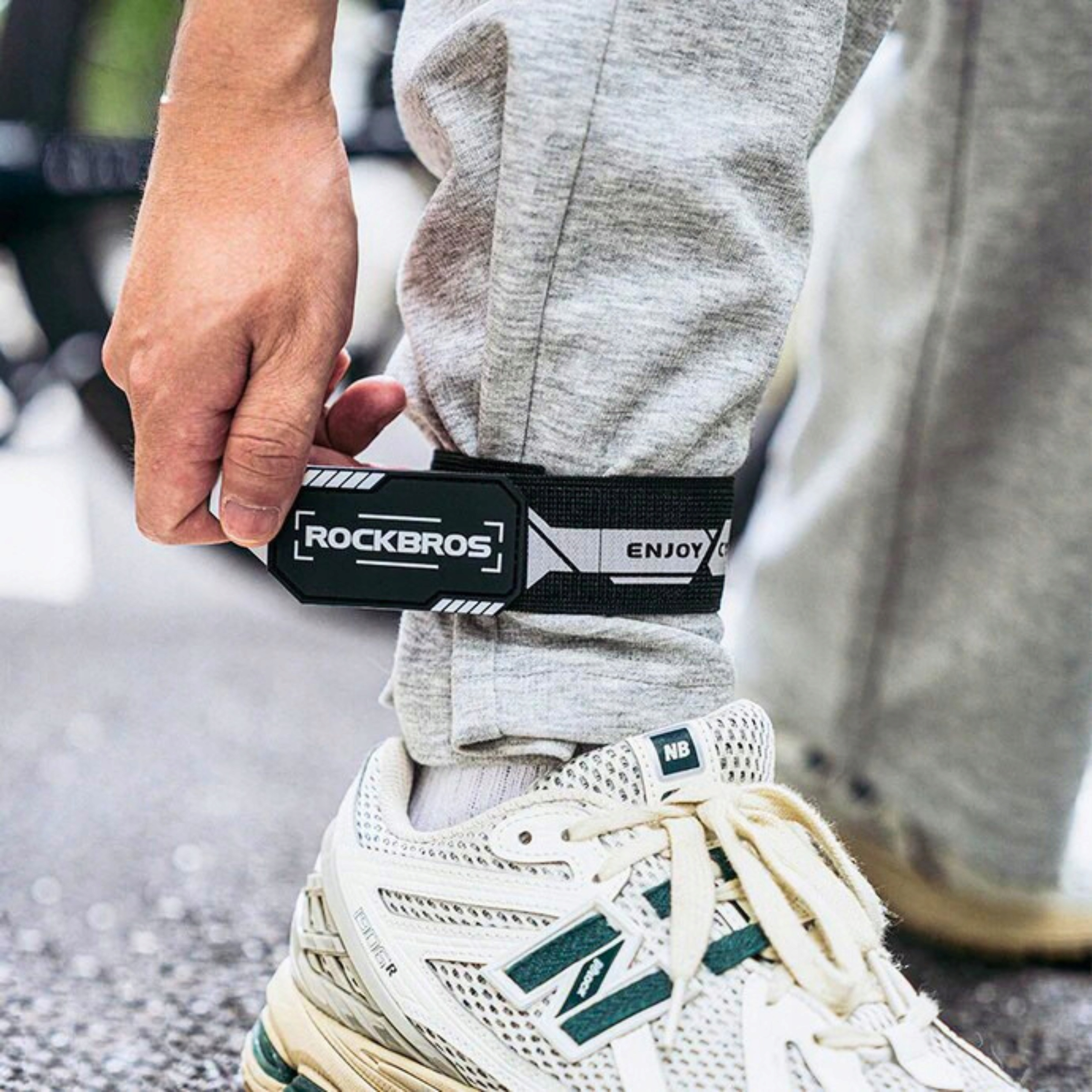 Noga osoby z opaską Rockbros wokół kostki. Osoba ma na sobie szare spodnie i trampki.