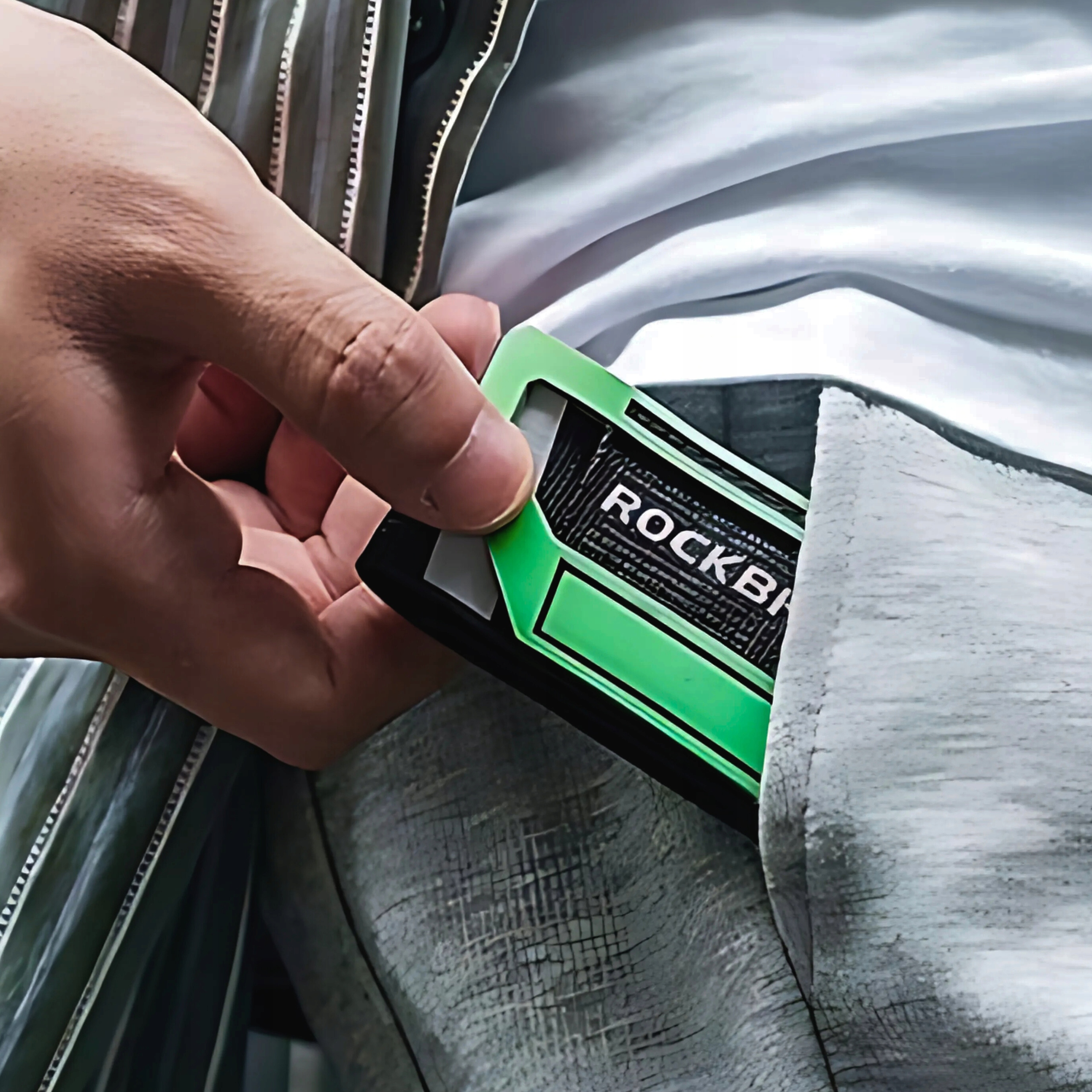 Dłoń trzymająca opaskę na kostkę Rockbros. Jest zielona i czarna. Ręka wkłada ją do kieszeni.