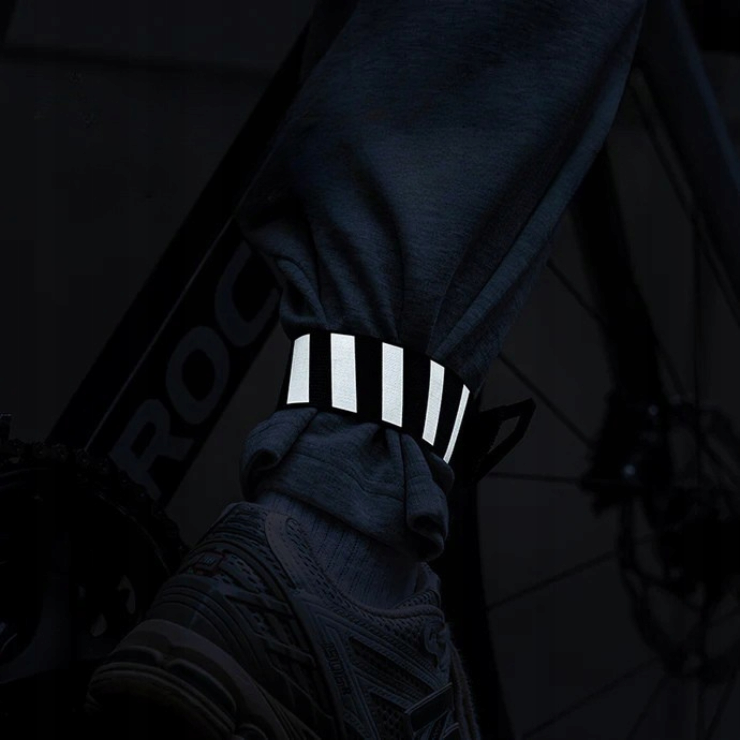 Osoba z odblaskową opaską na kostkę na rowerze. Opaska ma białe paski. Obraz jest ciemny.