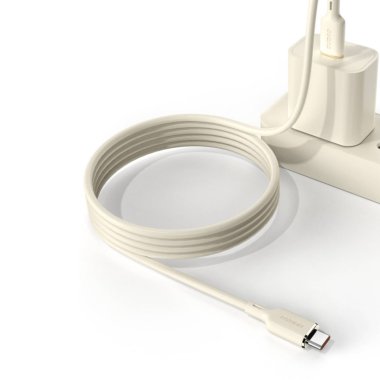 Kremowy kabel USB-C jest zwinięty i podłączony do ładowarki i białej listwy zasilającej, na białej powierzchni.