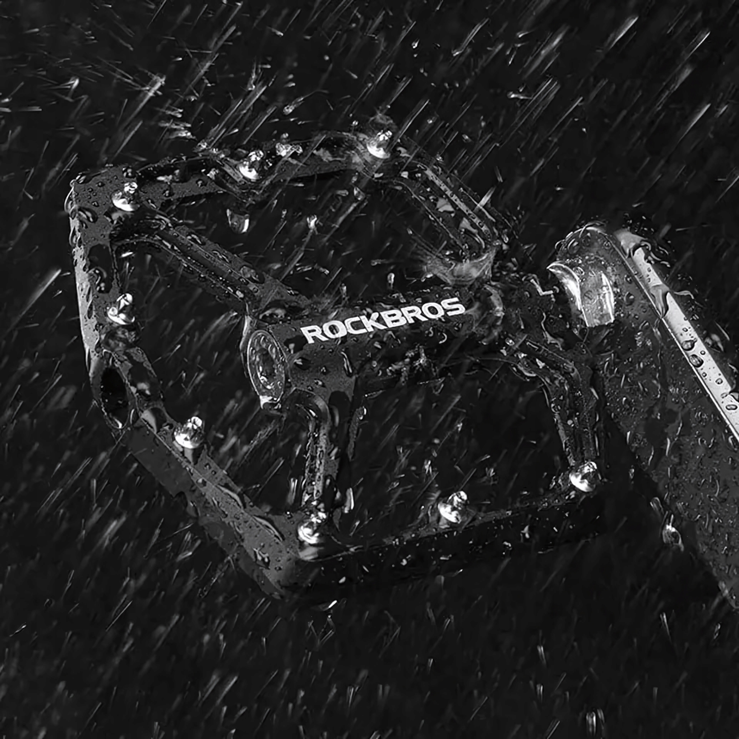 Czarny pedał rowerowy mokry z kroplami wody, pokazujący logo Rockbros.