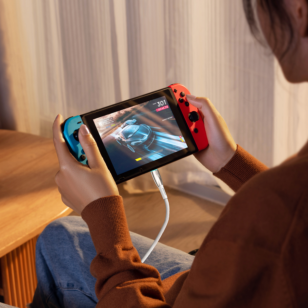 Osoba trzyma Nintendo Switch. Ekran wyświetla grę wyścigową. Joy-Cony są czerwone i niebieskie.