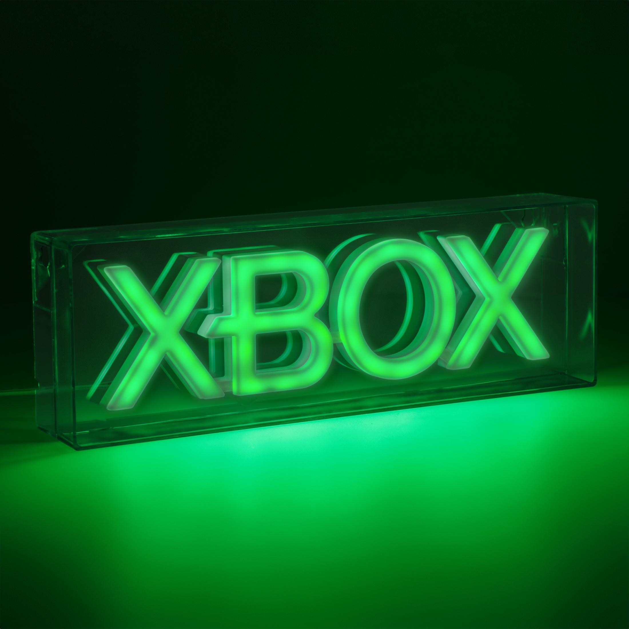 Zielony neonowy znak Xbox w przezroczystym pudełku, na zielonej powierzchni. Słowo XBOX świeci.