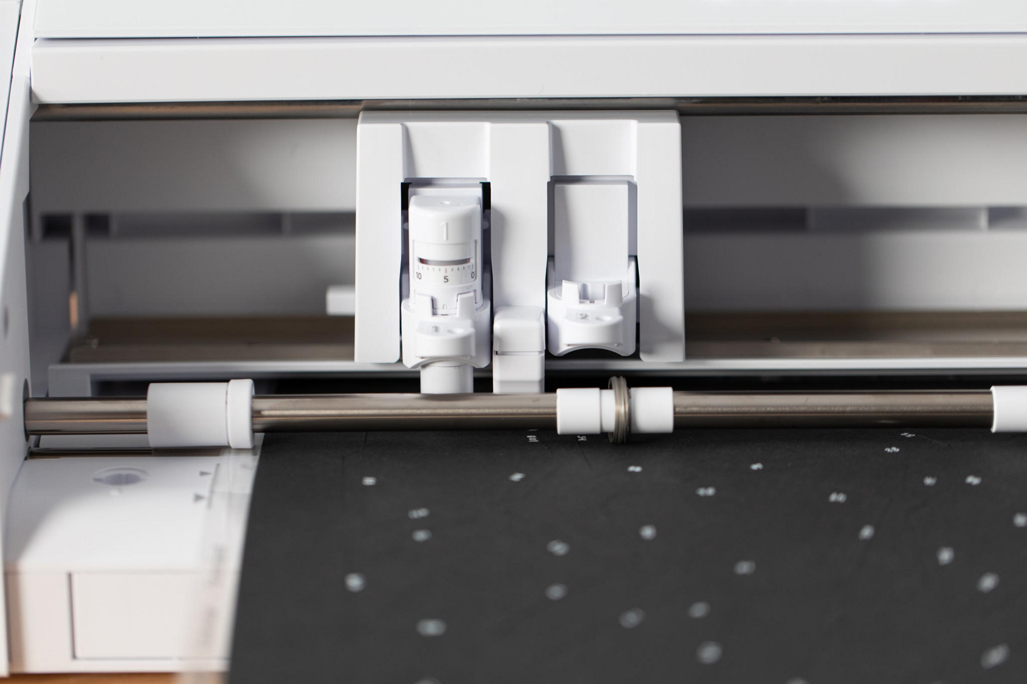 Eine weiße Schneidemaschine mit schwarzem Material darin und zwei weißen Einstellknöpfen.