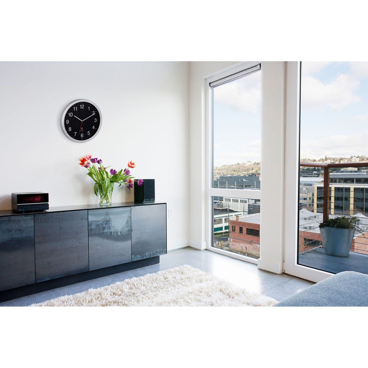 Stanza con orologio, mobile, fiori e finestra con vista su balcone e città.