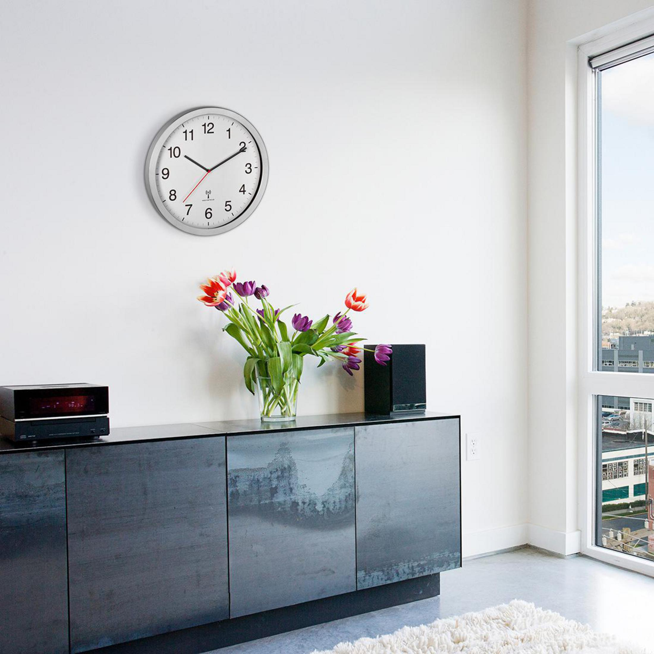 Ein Raum mit einer Uhr, Blumen in einer Vase und einem schwarzen Schrank. Rechts ist ein Fenster mit Aussicht.