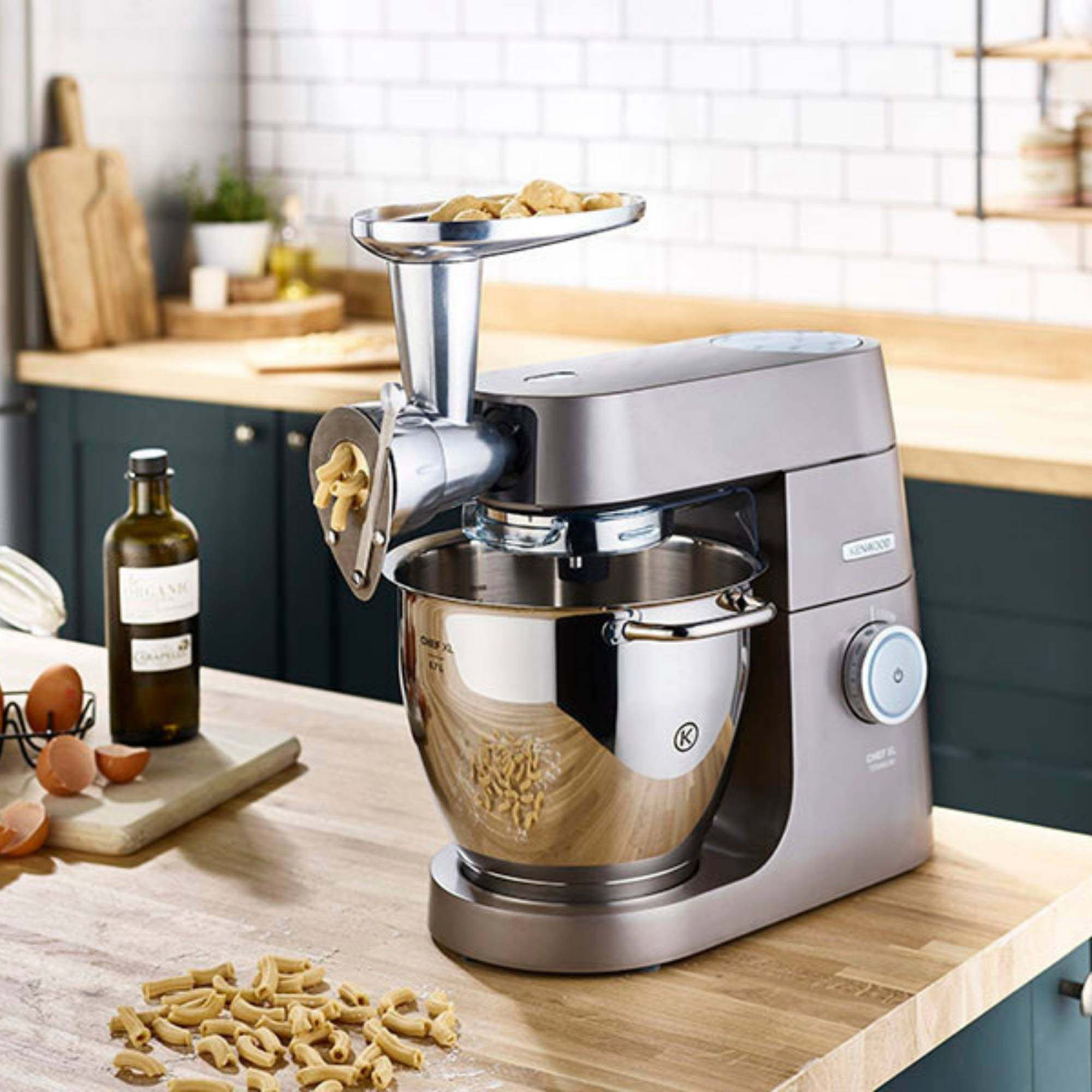Impastatrice da cucina con accessorio per pasta e pasta. Piano di lavoro in legno. Sfondo chiaro.