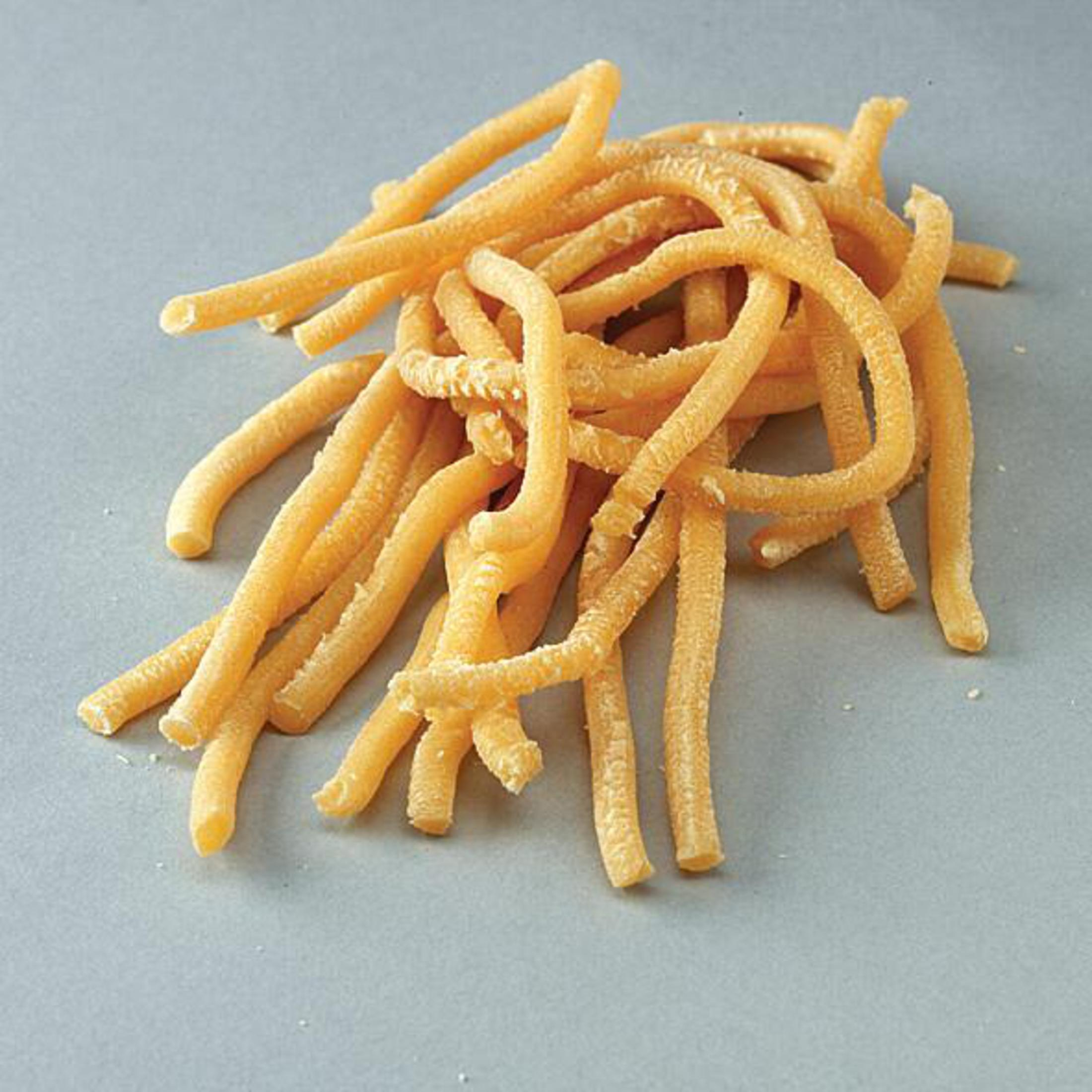 Un mucchio di pasta lunga e attorcigliata. Colore giallo pallido. Sfondo grigio.