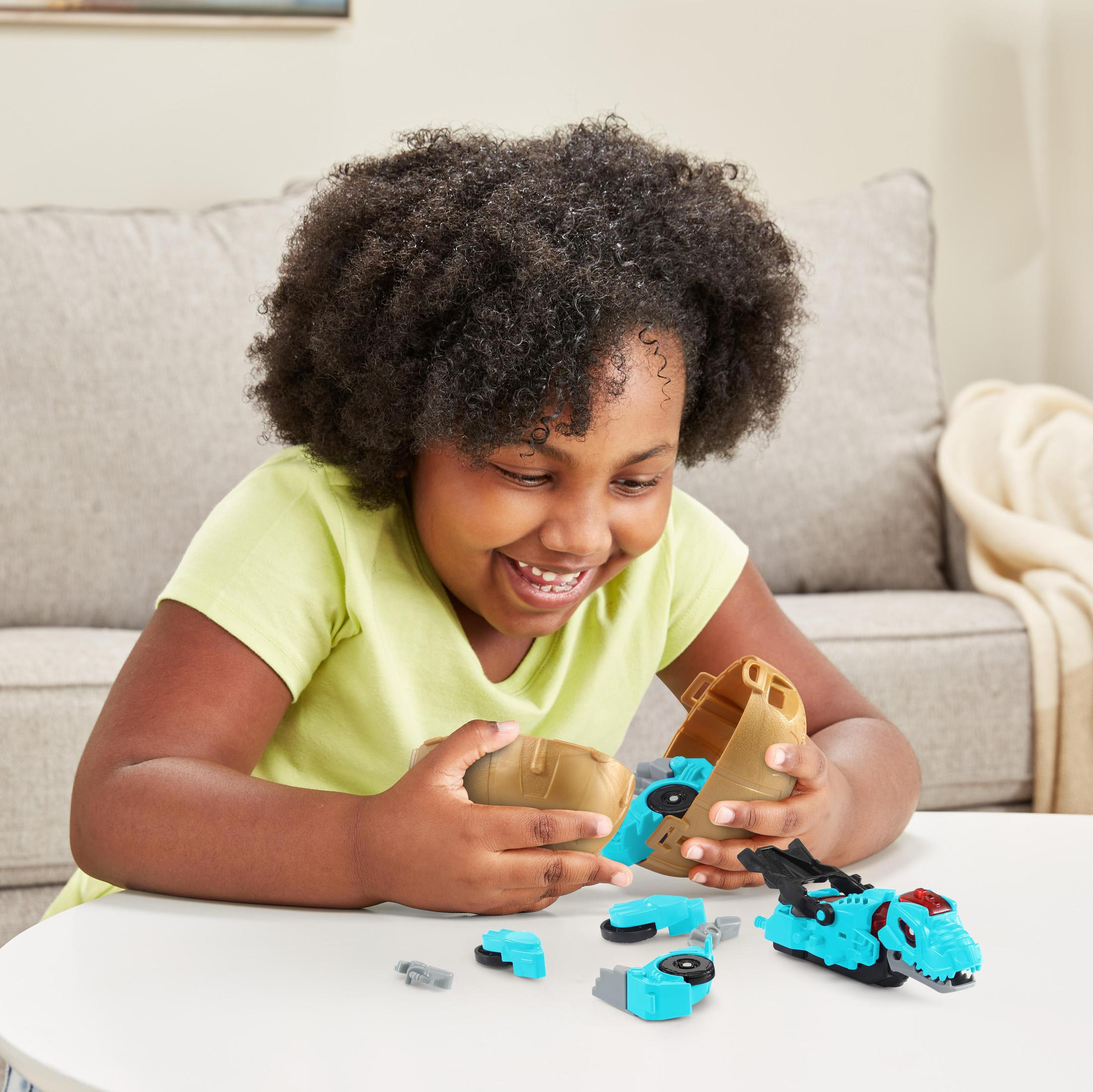 Ein Mädchen spielt mit einem Spielzeugdinosaurier. Sie sitzt an einem weißen Tisch, Spielzeugteile liegen auf dem Tisch.