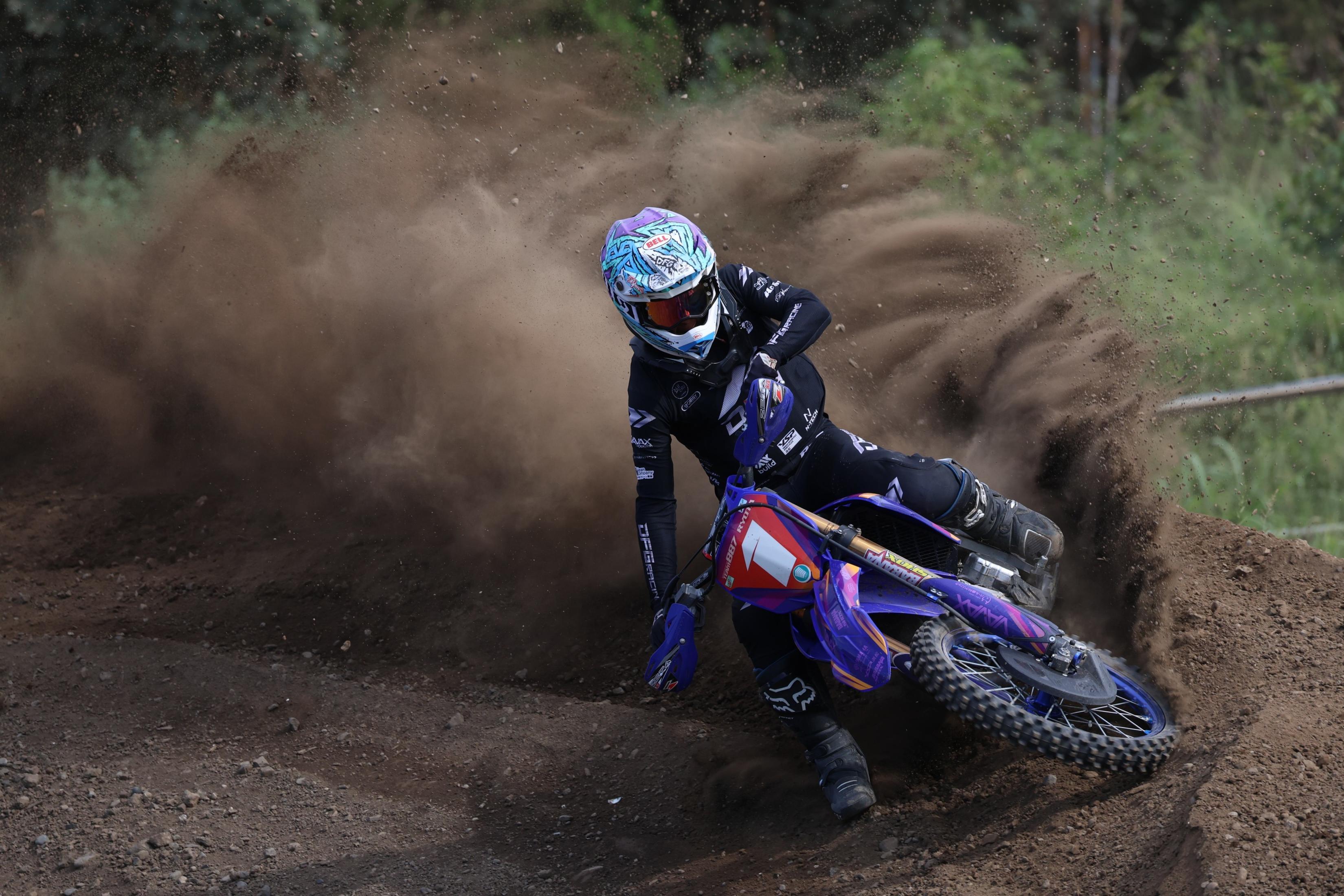 Motocross-Fahrer auf einer Dirt-Strecke, lehnt sich in eine Kurve, wirbelt Staub auf.