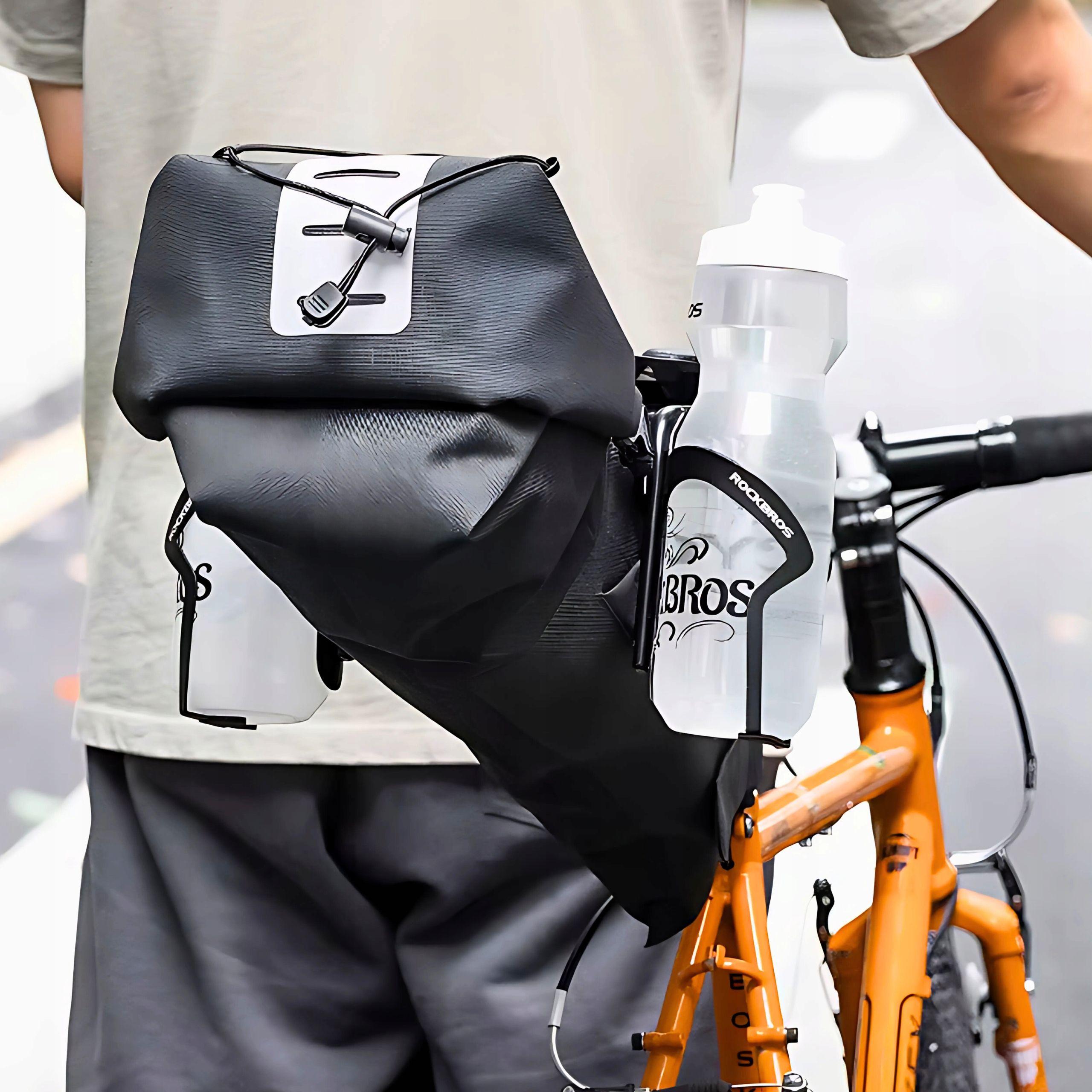 Osoba trzymająca rower z czarną torbą i dwiema butelkami na wodę. Torba jest czarno-biała.