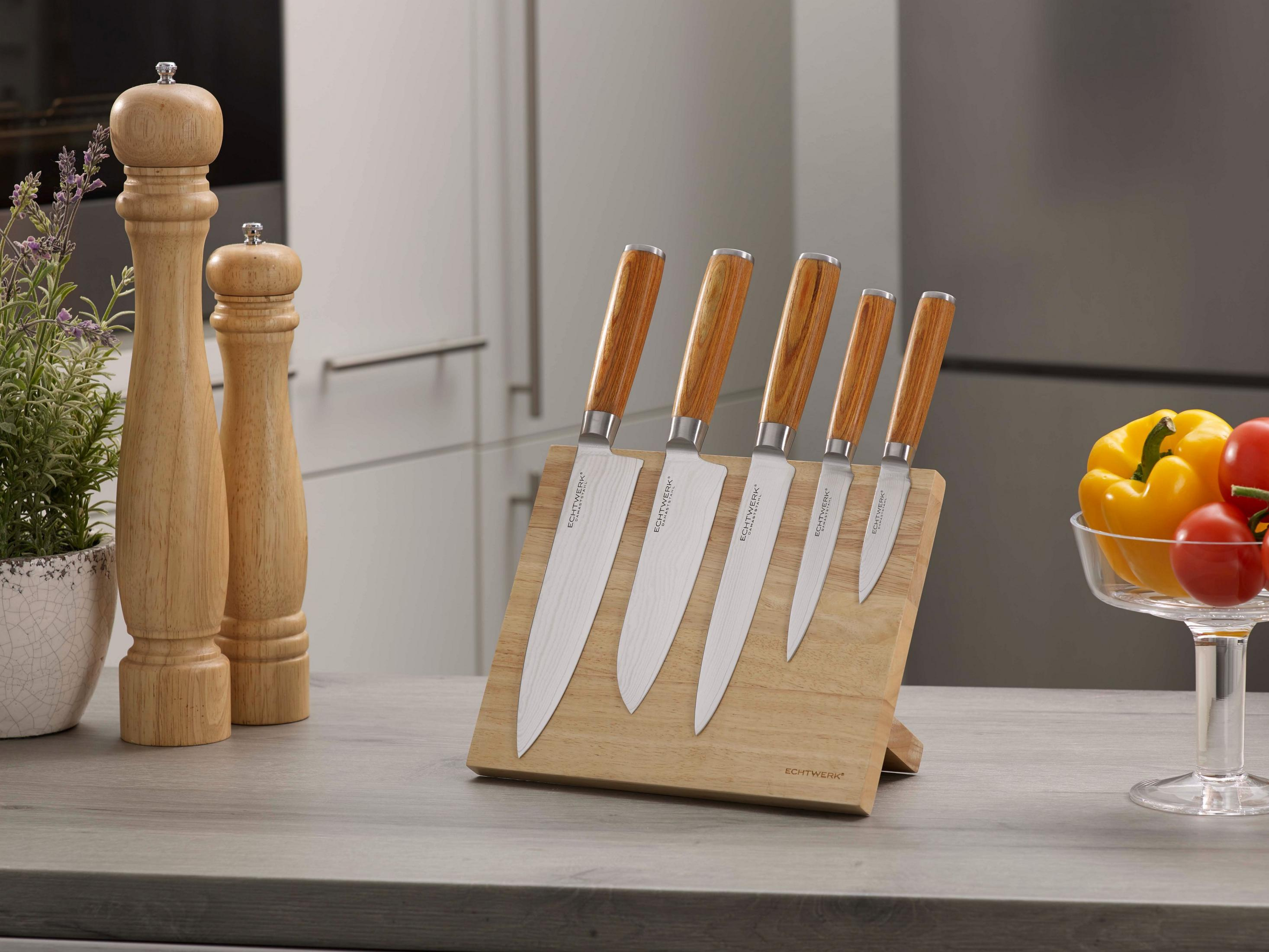 Küchenszene mit Messern auf einem Holzblock, Pfeffermühlen, Tomaten und einer gelben Paprika.