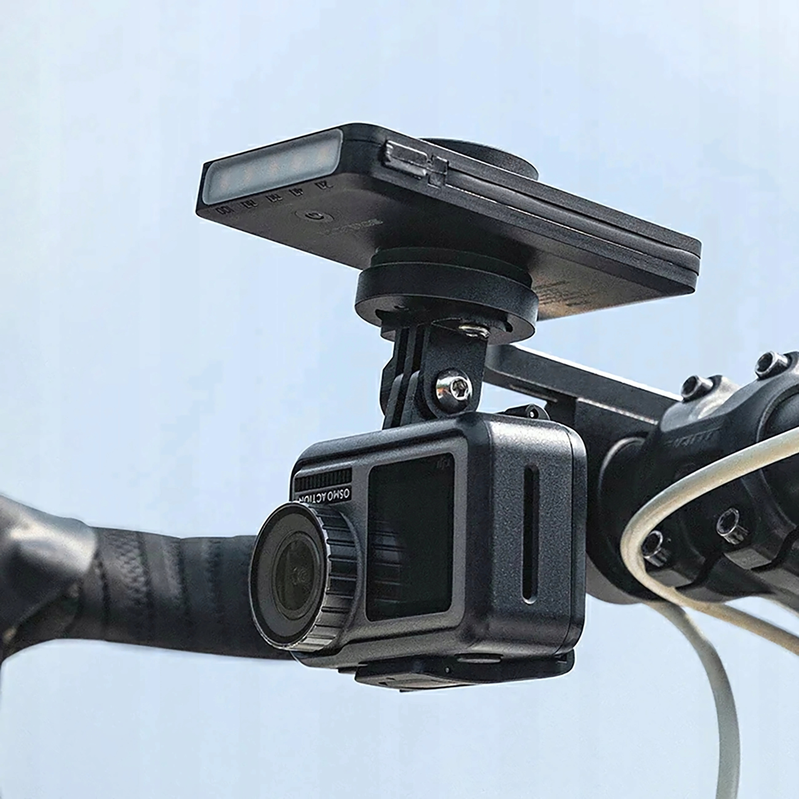 Czarna kamera sportowa na kierownicy roweru. Kamera jest zamontowana na wsporniku. Tłem jest niebo.