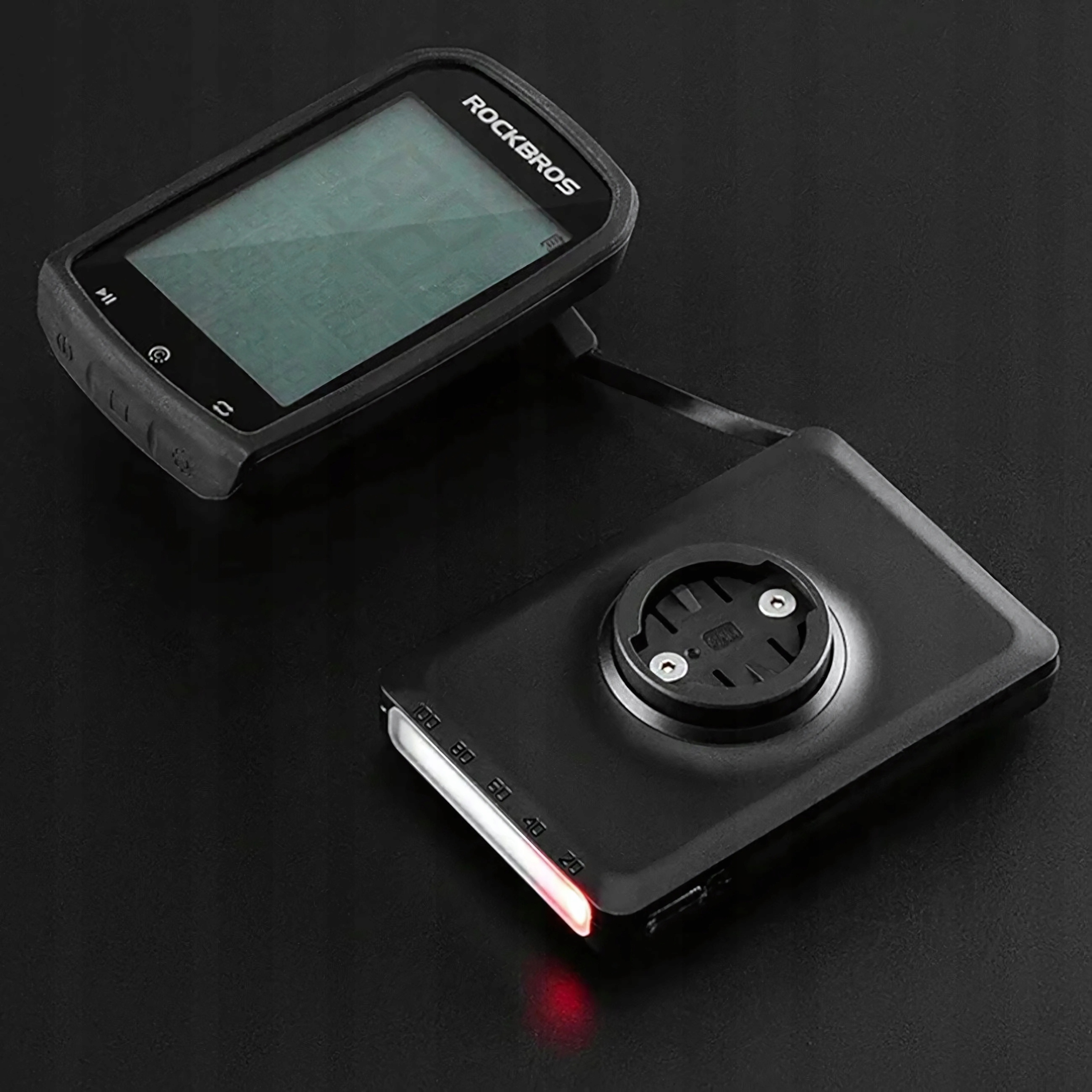 Czarne urządzenie z logo Rockbros i komputerem rowerowym na ciemnej powierzchni. Świeci się czerwone światło.