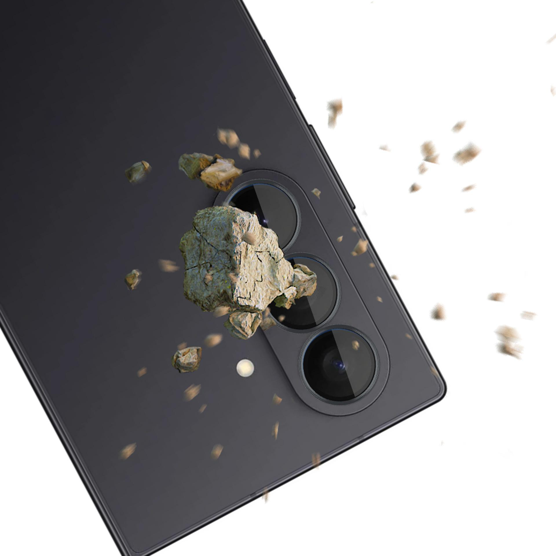 Czarny telefon z trzema tylnymi aparatami. Małe kamienie spadają, sugerując test wytrzymałości na białym tle.