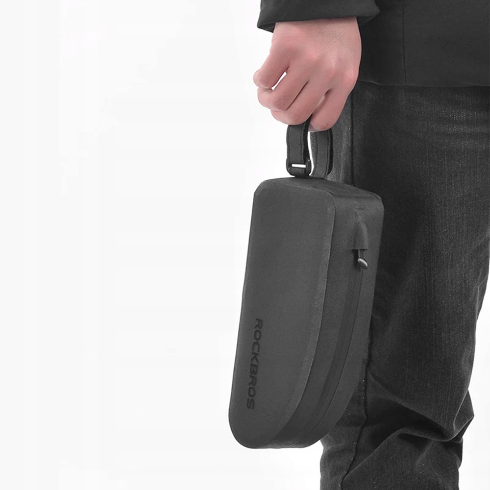 Osoba trzyma czarną, prostokątną torbę z napisem ROCKBROS. Tłem jest biała ściana.