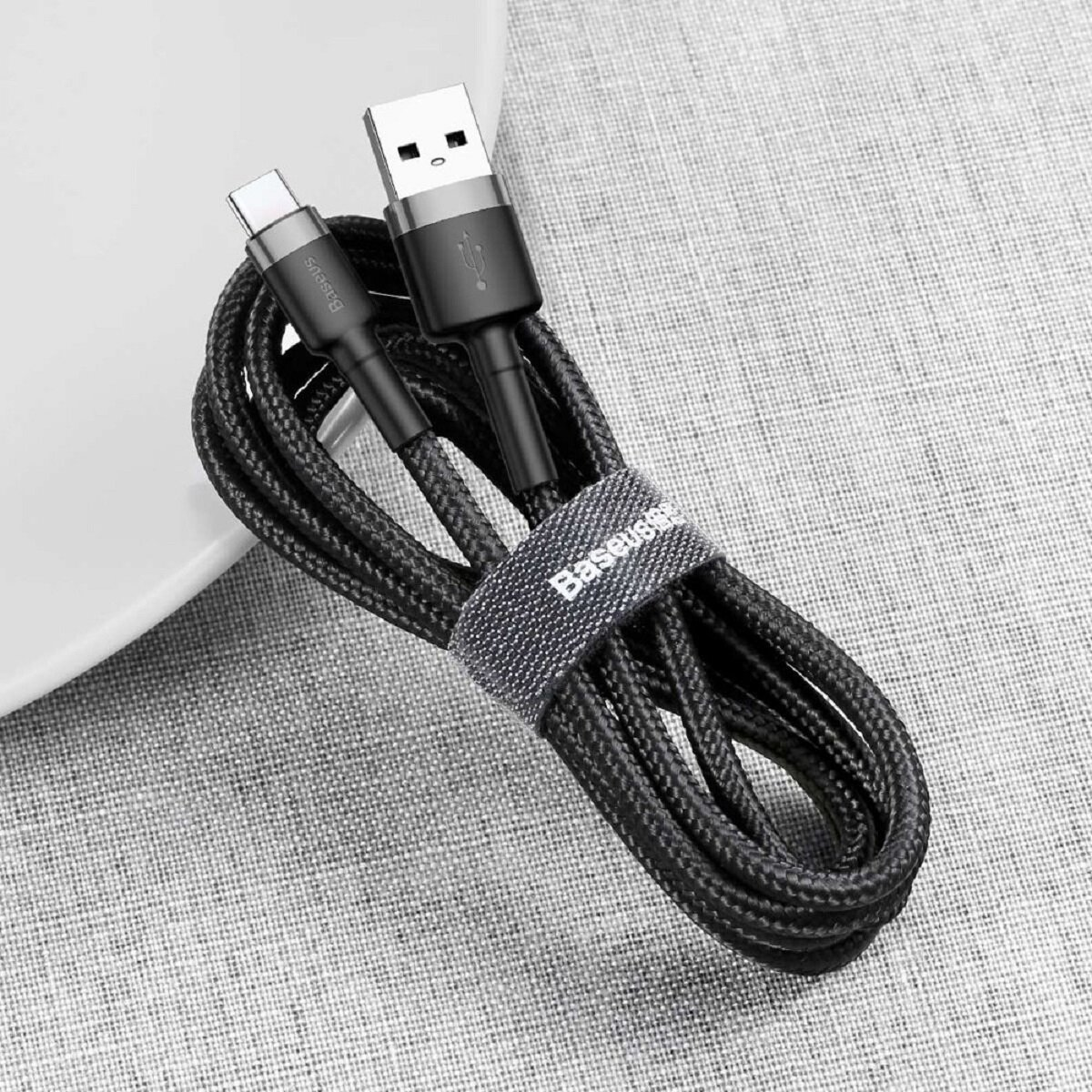 Zwinięty czarny kabel USB do Type-C z logo Baseus i plecioną teksturą. Białe tło.