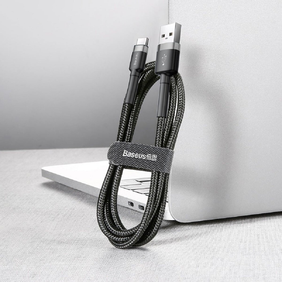 Czarny kabel USB ze złączami USB-A i USB-C, owinięty czarnym paskiem, obok laptopa.