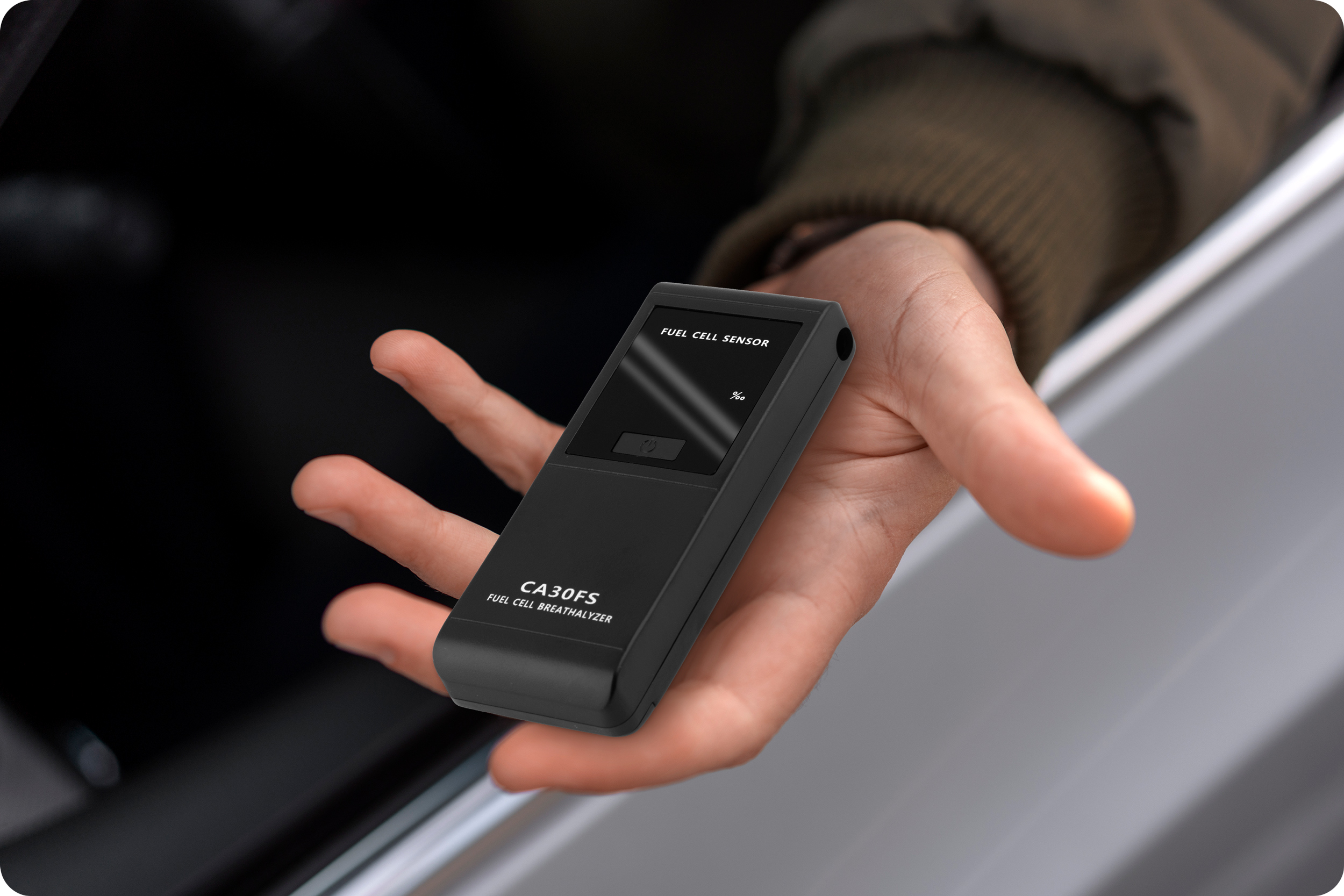 Ręka trzyma alkomat, pokazując na ekranie 0,00%. Ręka jest w samochodzie.