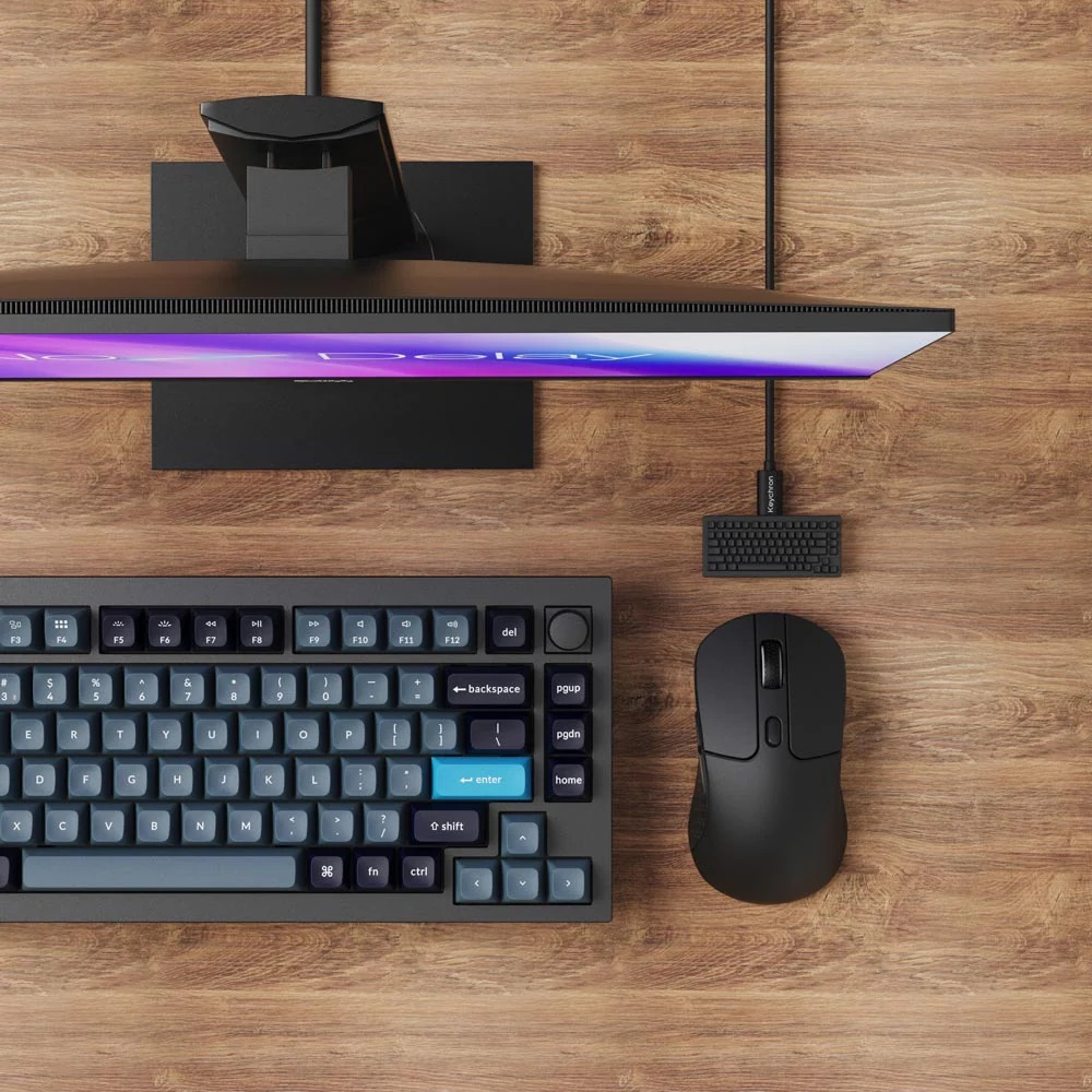 Czarna mysz, klawiatura i monitor na drewnianej powierzchni.