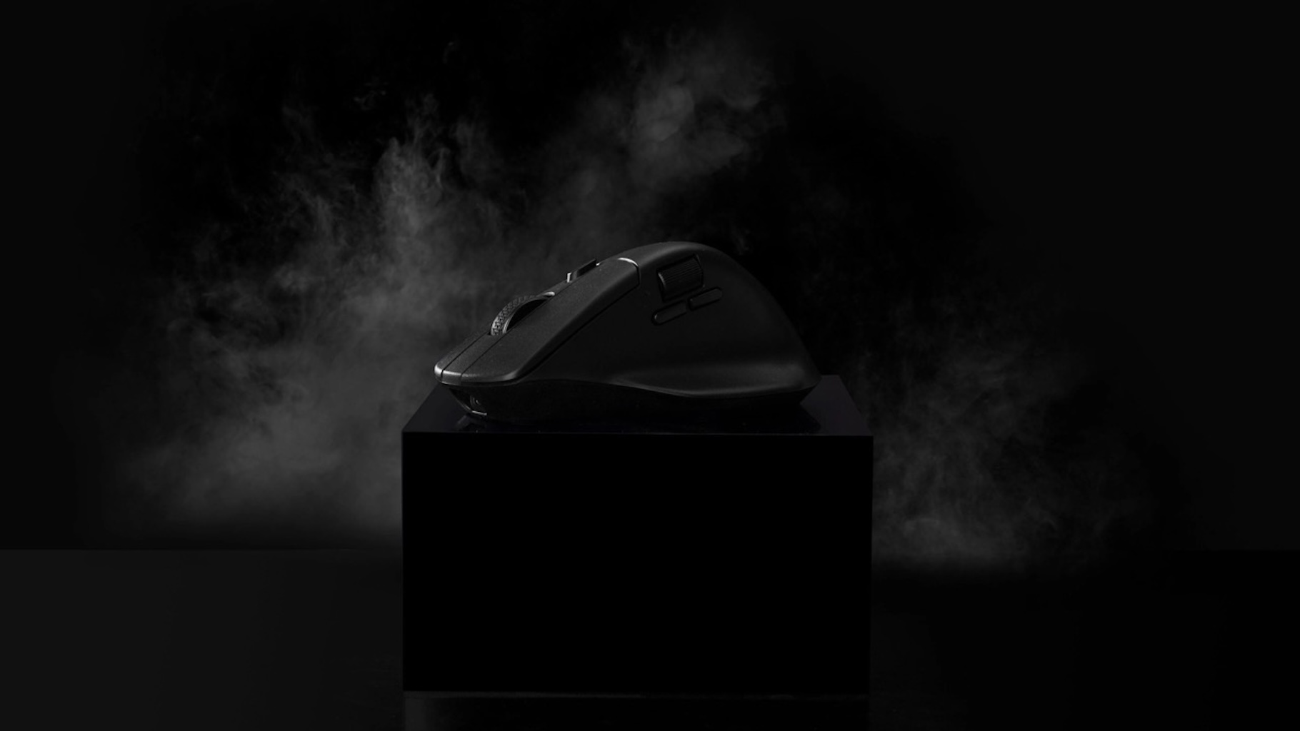 Czarna mysz komputerowa na czarnym stojaku, na zadymionym czarnym tle.