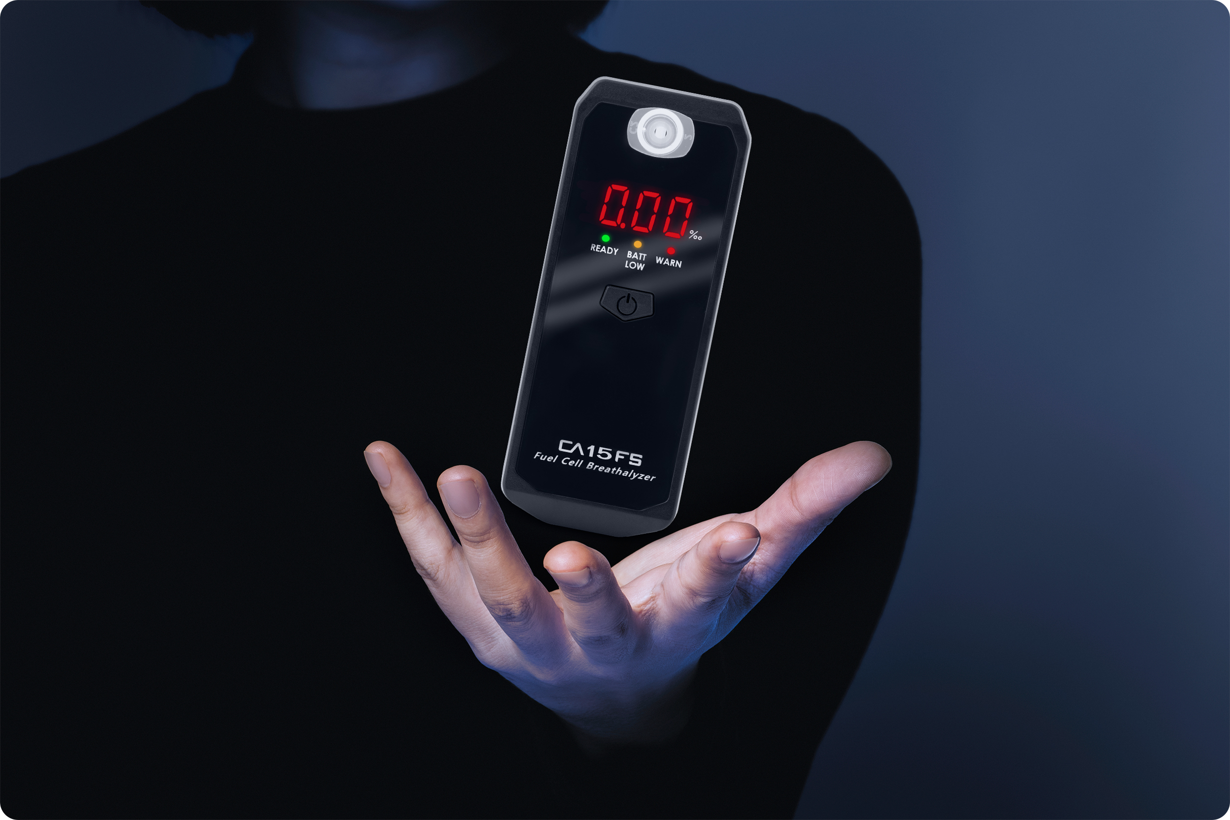 Ręka trzyma alkomat z wyświetlonym '0.00'. Tło jest rozmyte niebieskie, alkomat jest ostry.