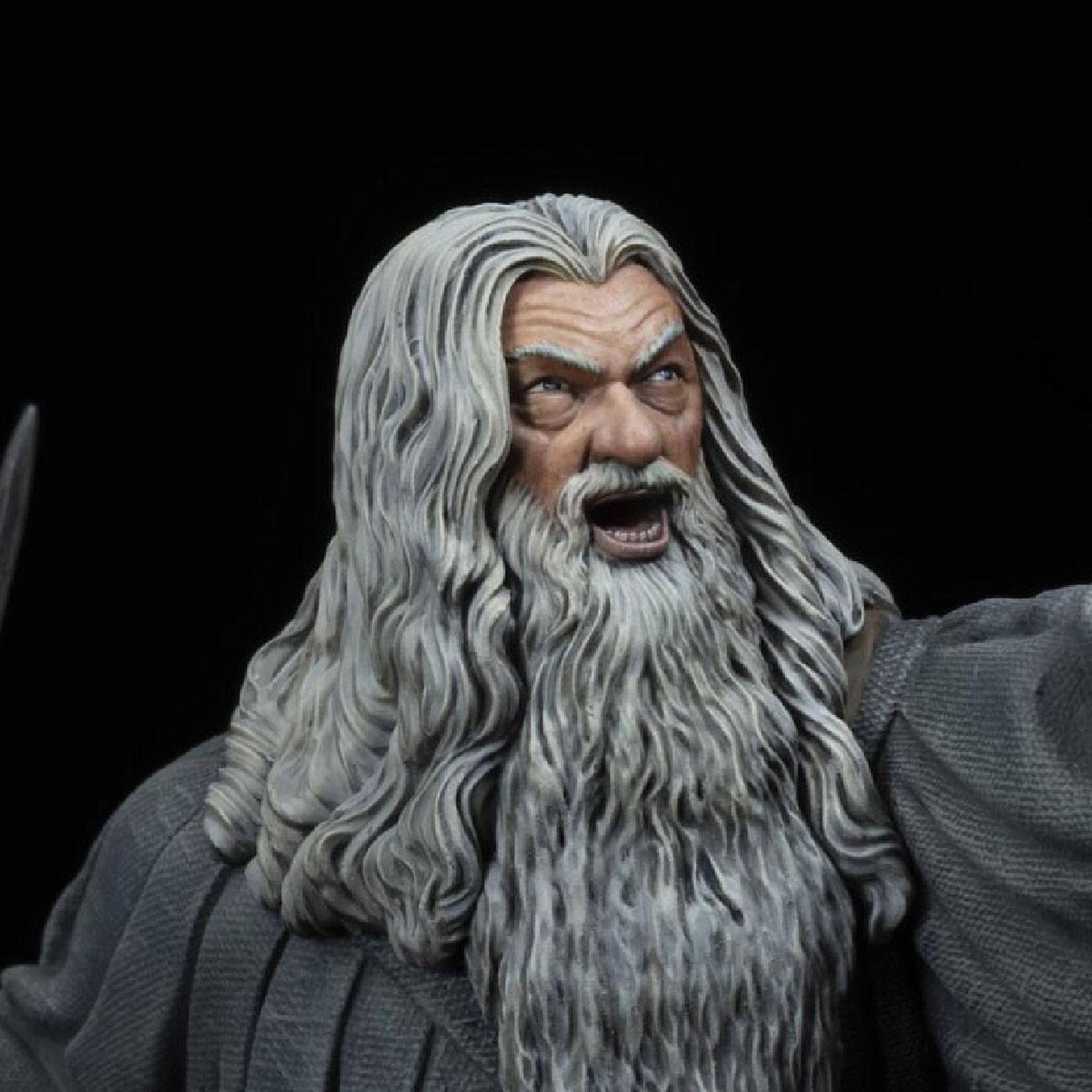 Primer plano de la cara de Gandalf. Barba blanca, pelo gris, boca abierta y ojos azules. Fondo oscuro.
