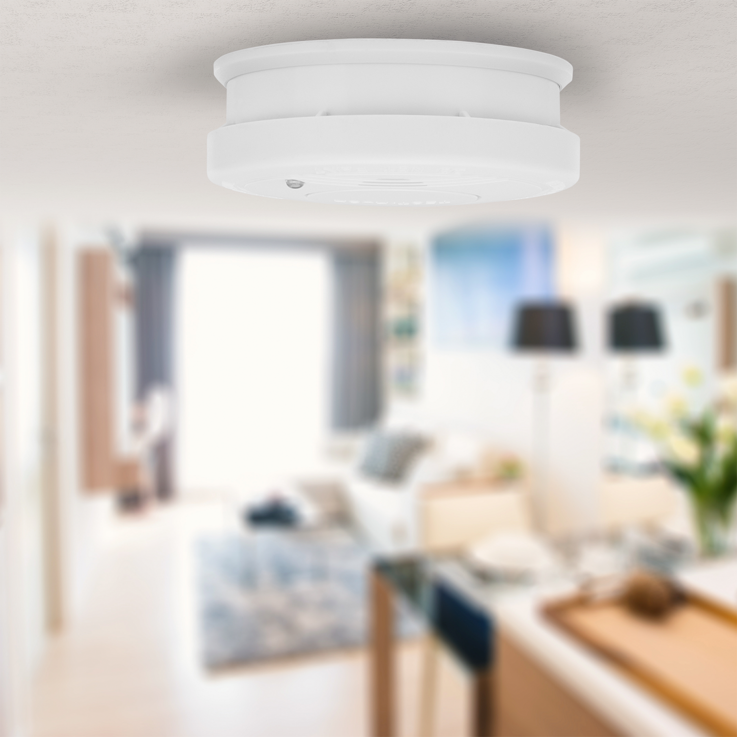 Un rilevatore di fumo bianco sul soffitto. Lo sfondo è un soggiorno sfocato.