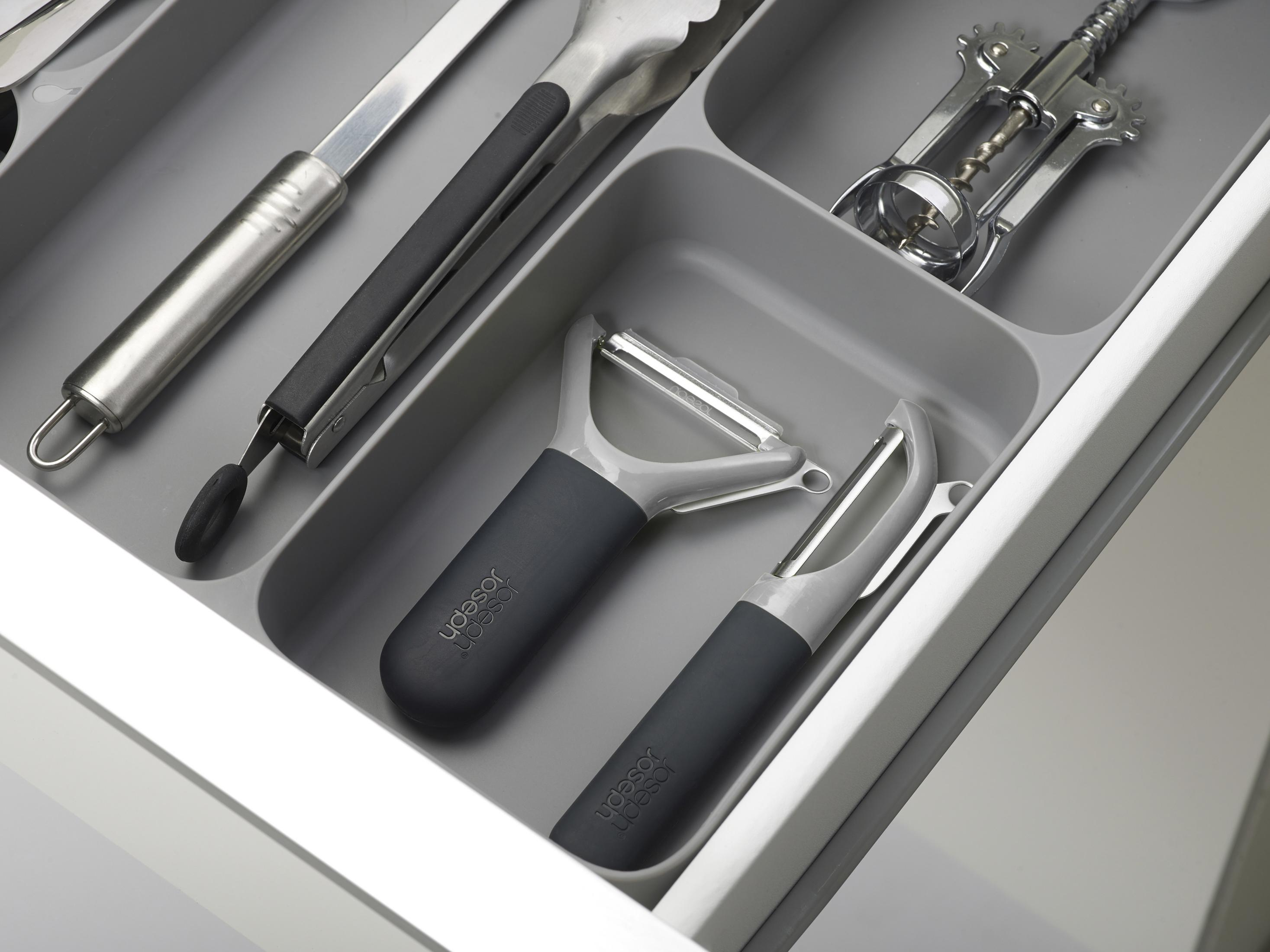 Un cajón con utensilios de cocina: espátula, pinzas, abrelatas y dos peladores.