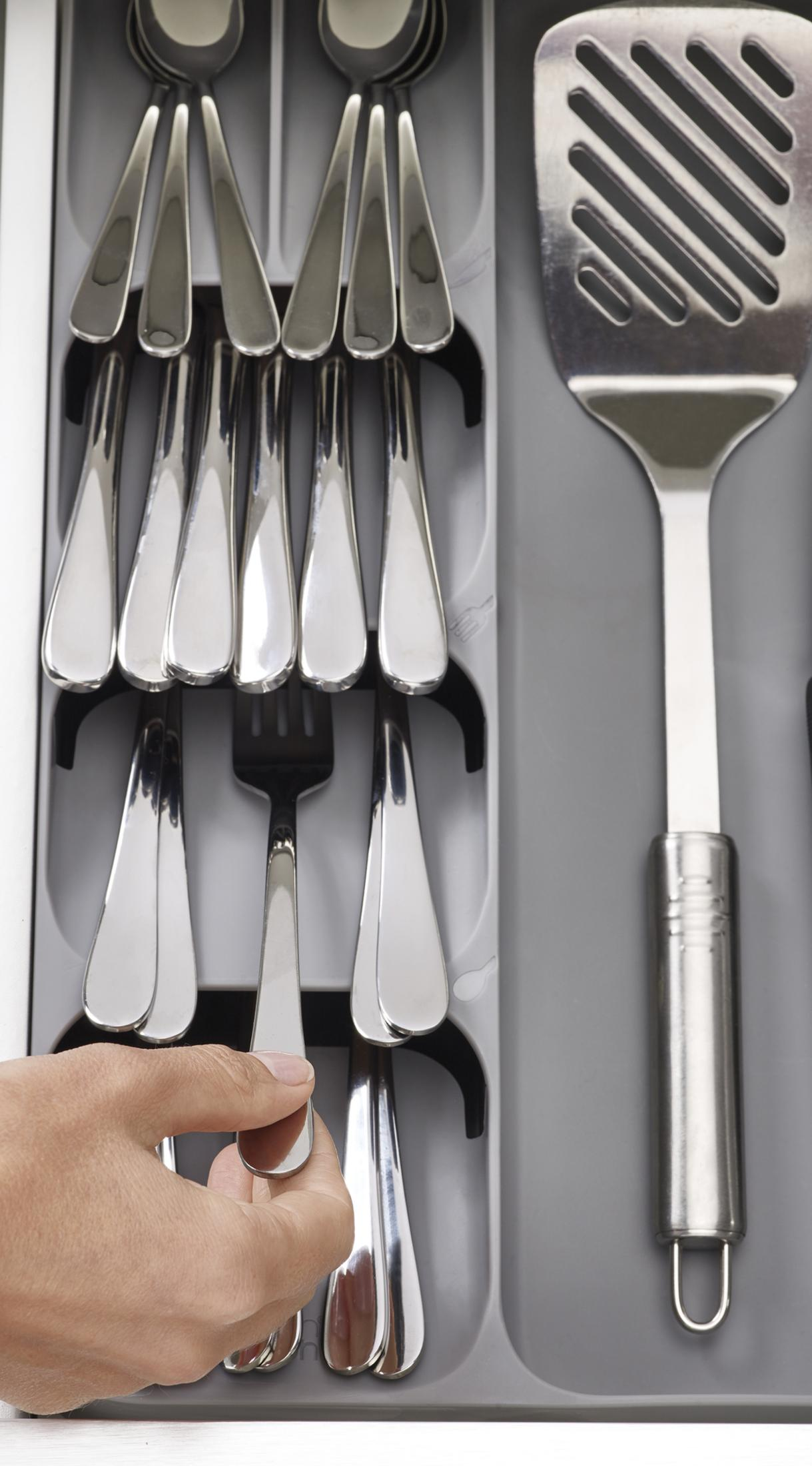 Un cajón con cubiertos. Una mano alcanza un tenedor. Predominan los colores gris y blanco.