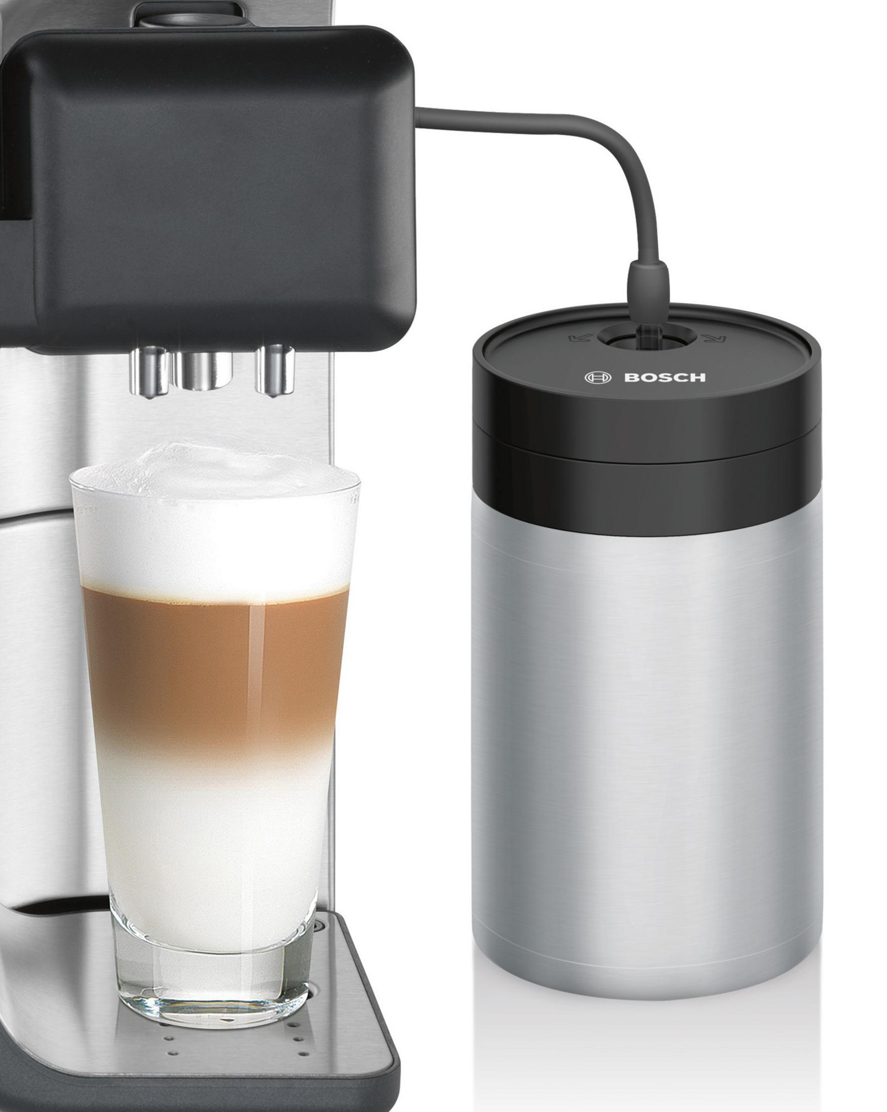 Ein Latte in einem Glas neben einem silbernen und schwarzen Bosch-Zylinder, Teil einer Kaffeemaschine.