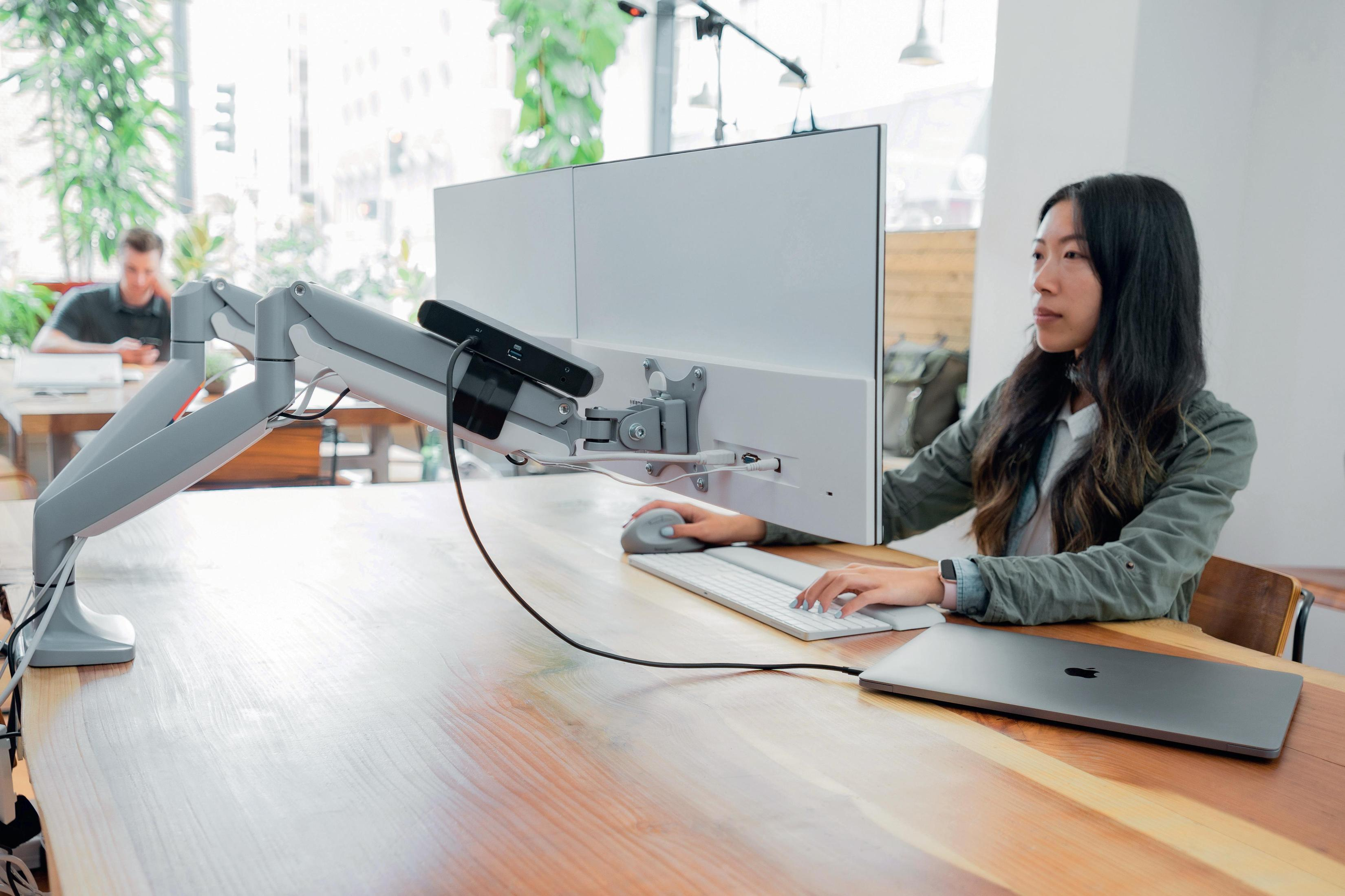 Eine Frau, die einen Computer mit Monitorarmen an einem Holztisch benutzt.