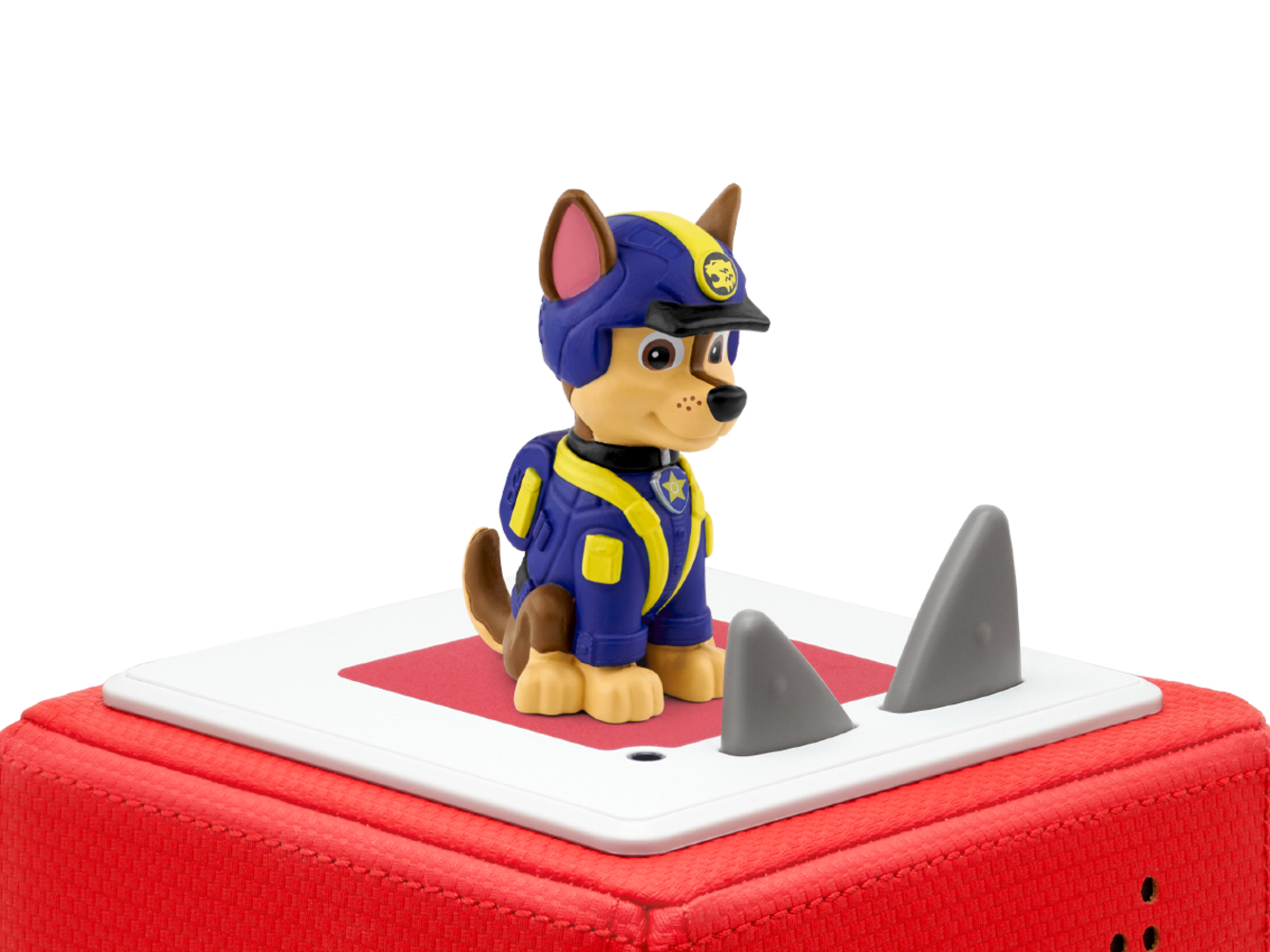 Eine Paw Patrol Chase-Figur auf einer rot-weißen Plattform, mit Haifischflossen und weißem Hintergrund.