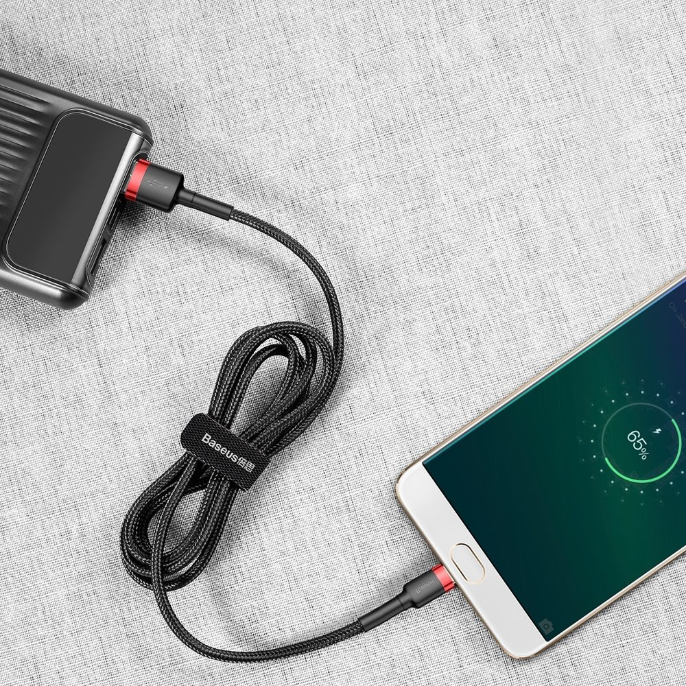 Telefon ładujący się czarnym kablem USB, podłączony do power banku i smartfona z 65% naładowania.