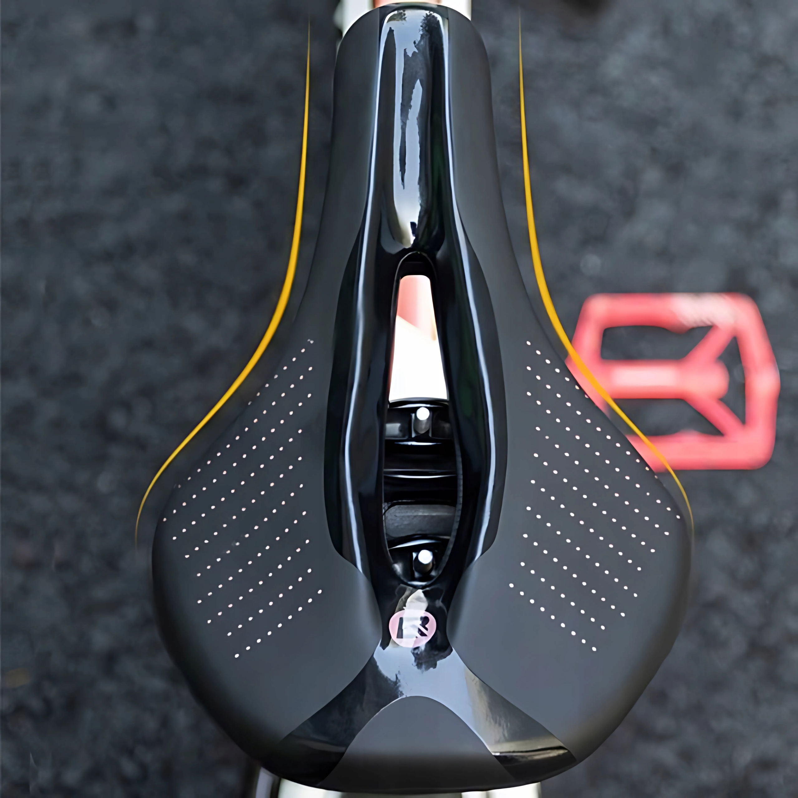 Czarne siodełko rowerowe z białymi kropkami. Czerwony pedał w tle.