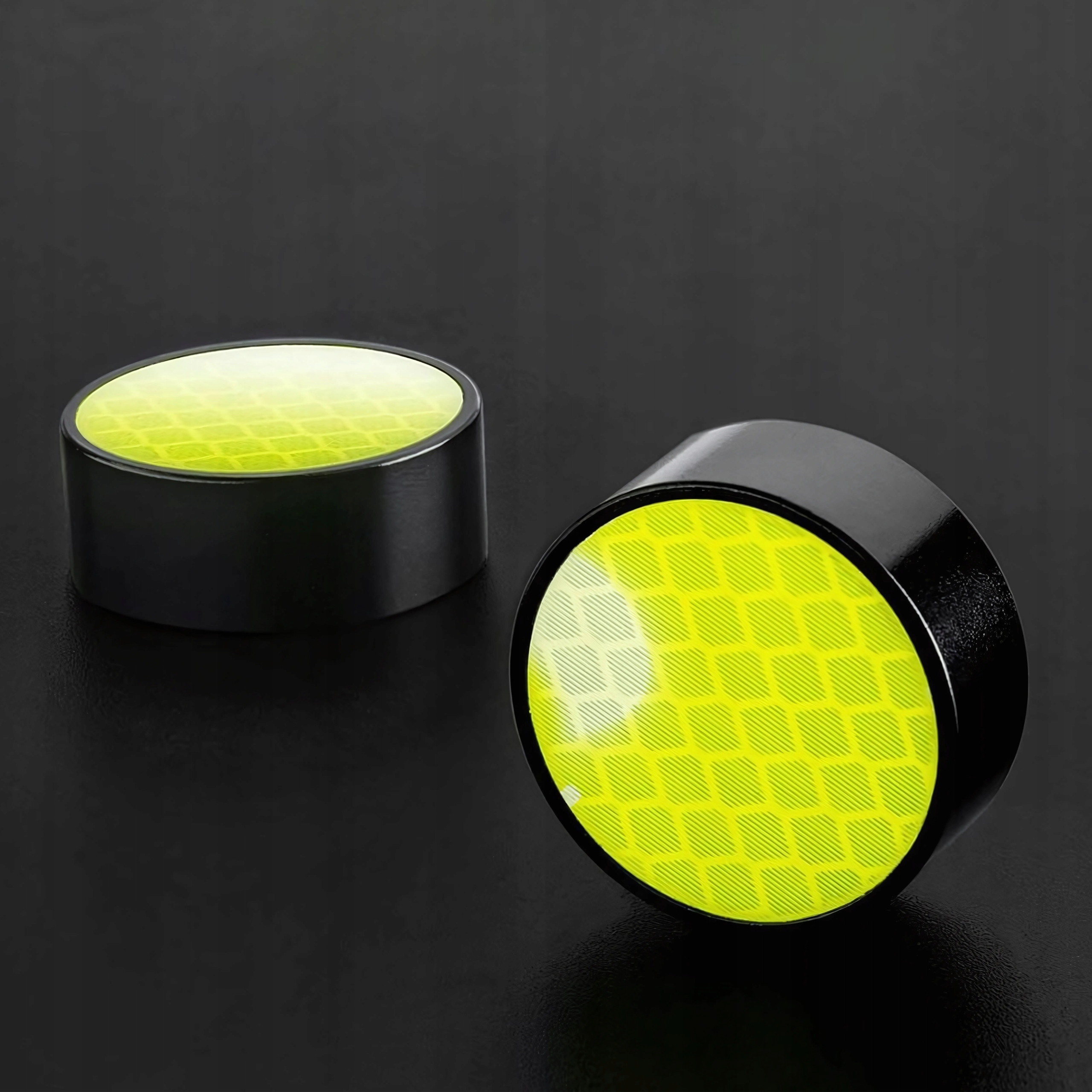 Dwie czarne nasadki z żółtymi odblaskami na ciemnej powierzchni. Jedna pionowo, druga poziomo.