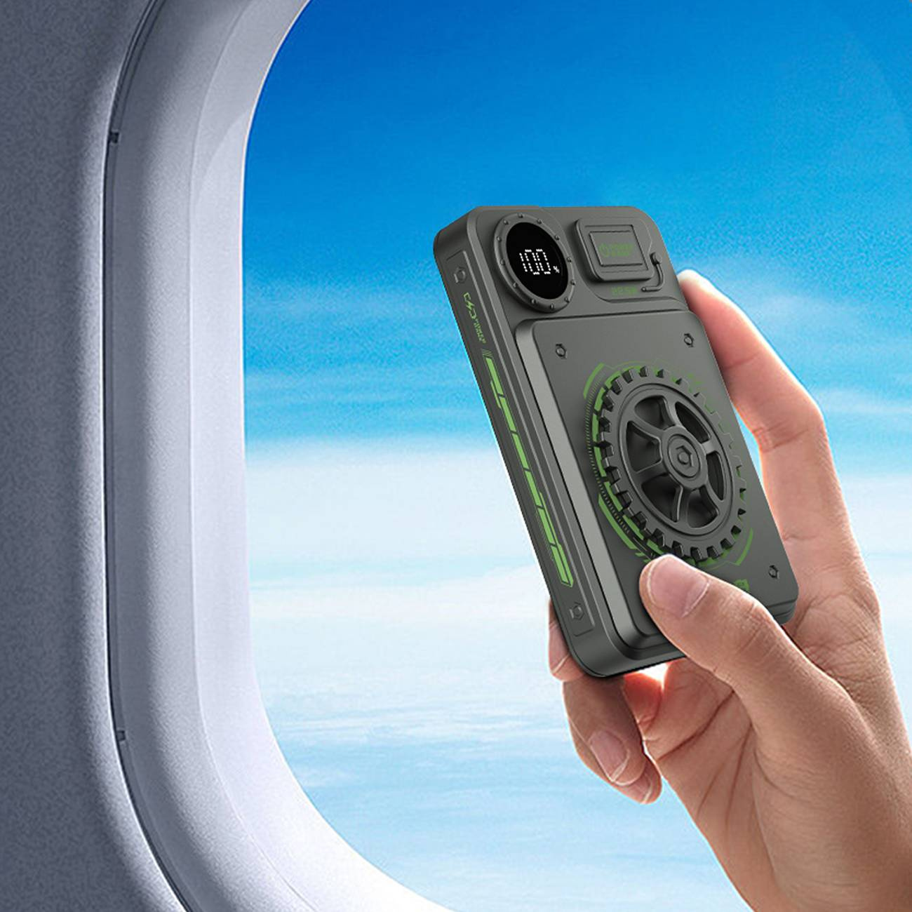 Dłoń trzymająca power bank. Power bank jest zielono-szary, pokazuje 100% naładowania.