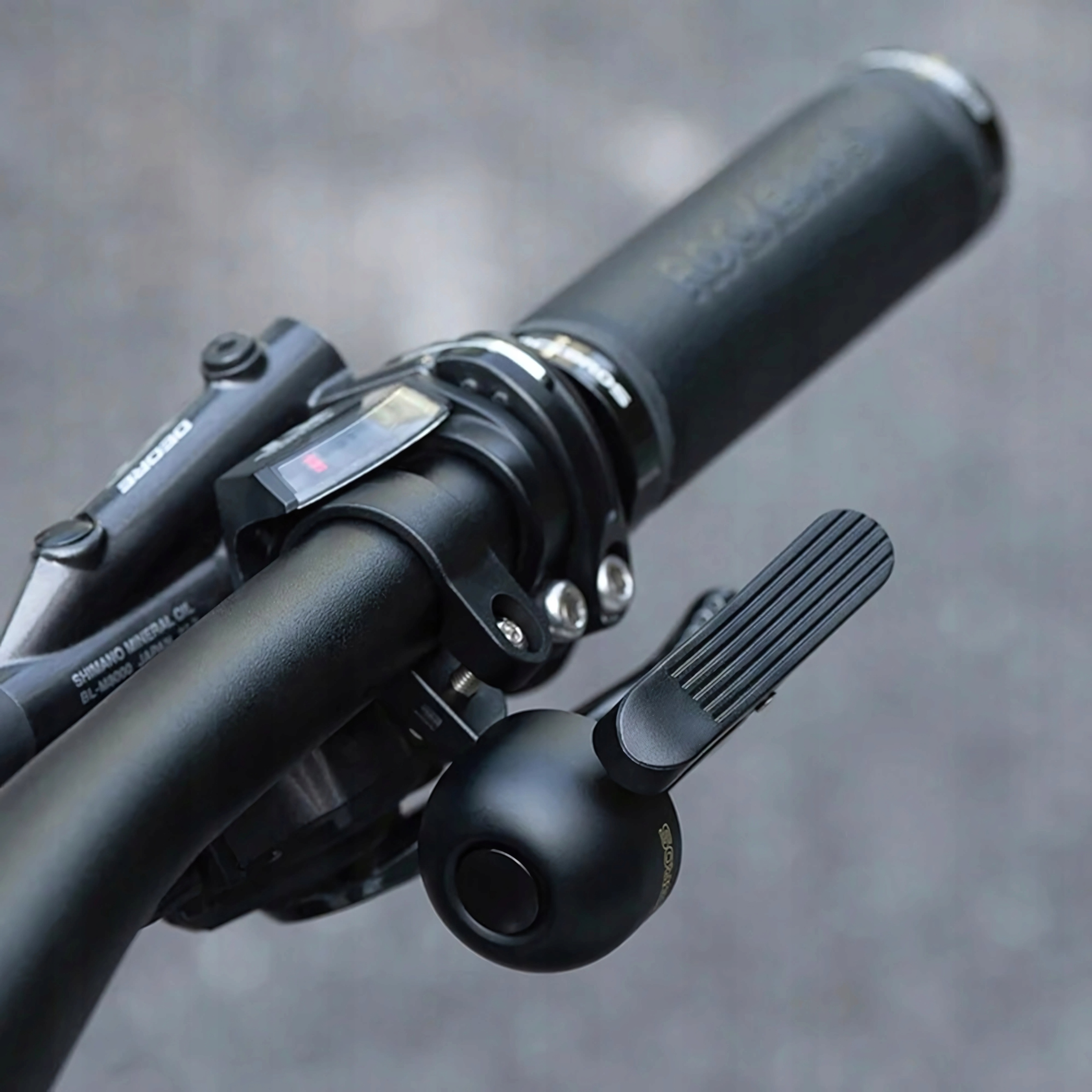 Dzwonek rowerowy zamontowany na kierownicy. Dzwonek jest czarny, z marką ROCKBROS.