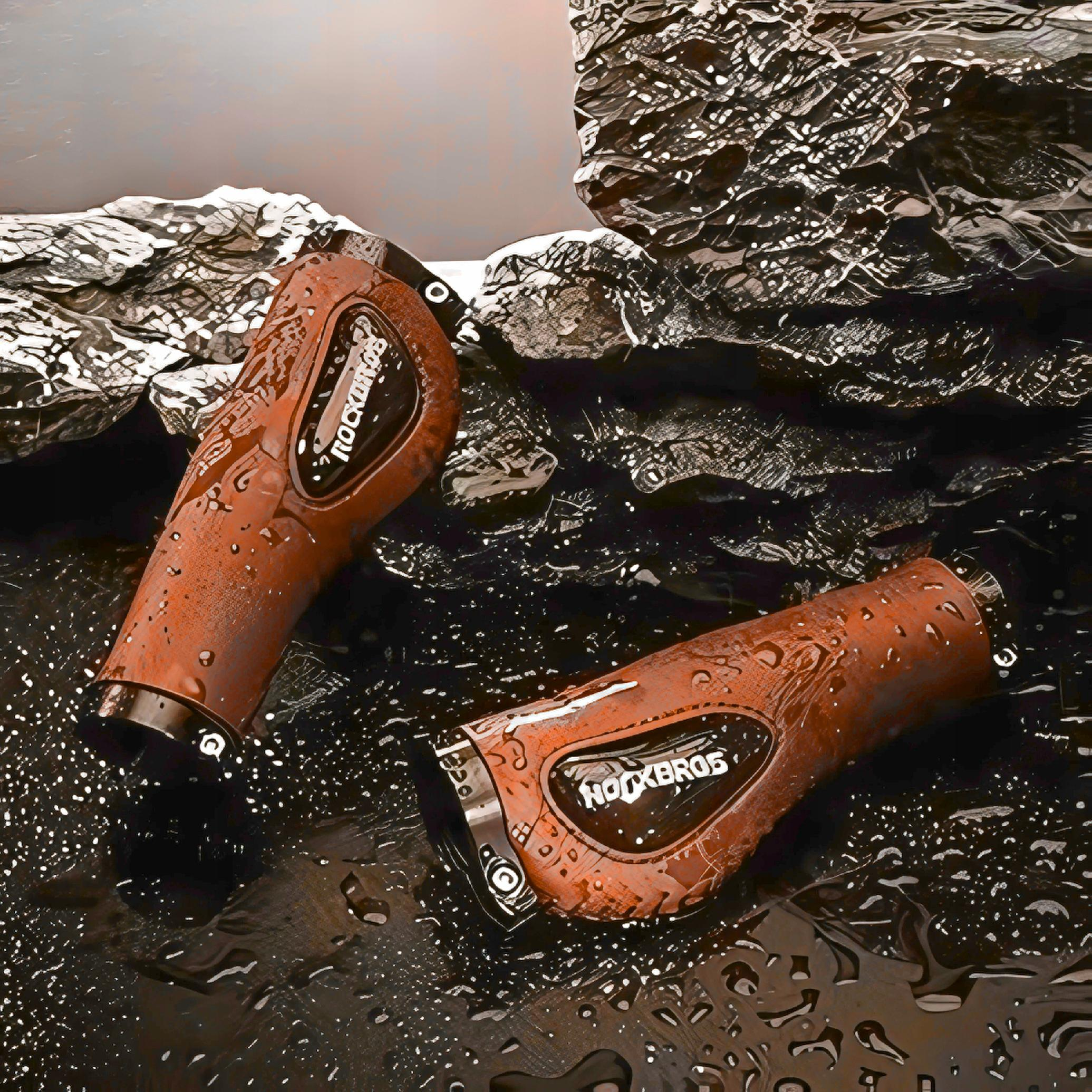 Dwa brązowe uchwyty kierownicy rowerowej z logo Rockbros na mokrej, ciemnej powierzchni.