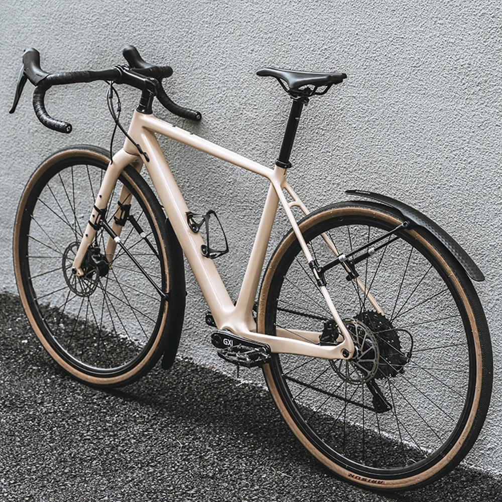 Beżowy rower opiera się o szarą ścianę. Rower ma czarną kierownicę i brązowe opony.