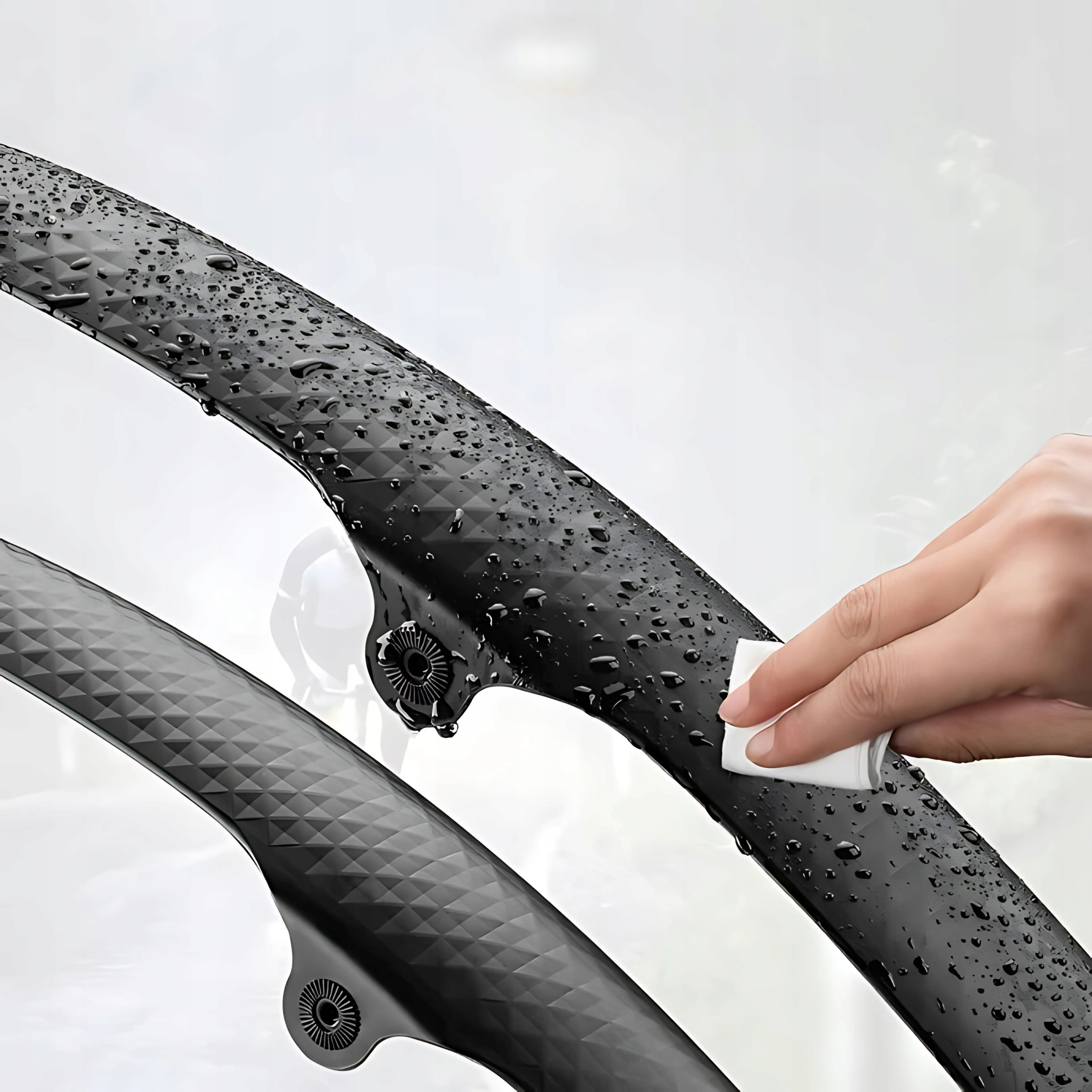 Ręka wyciera czarny błotnik rowerowy białą szmatką, pokazując krople wody na błotniku.