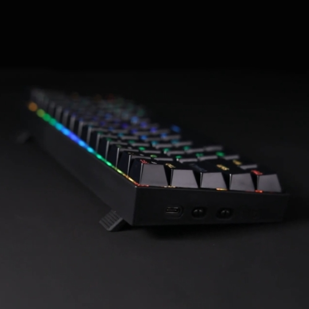 Teclado negro con teclas coloridas en superficie negra, vista lateral, inclinado.