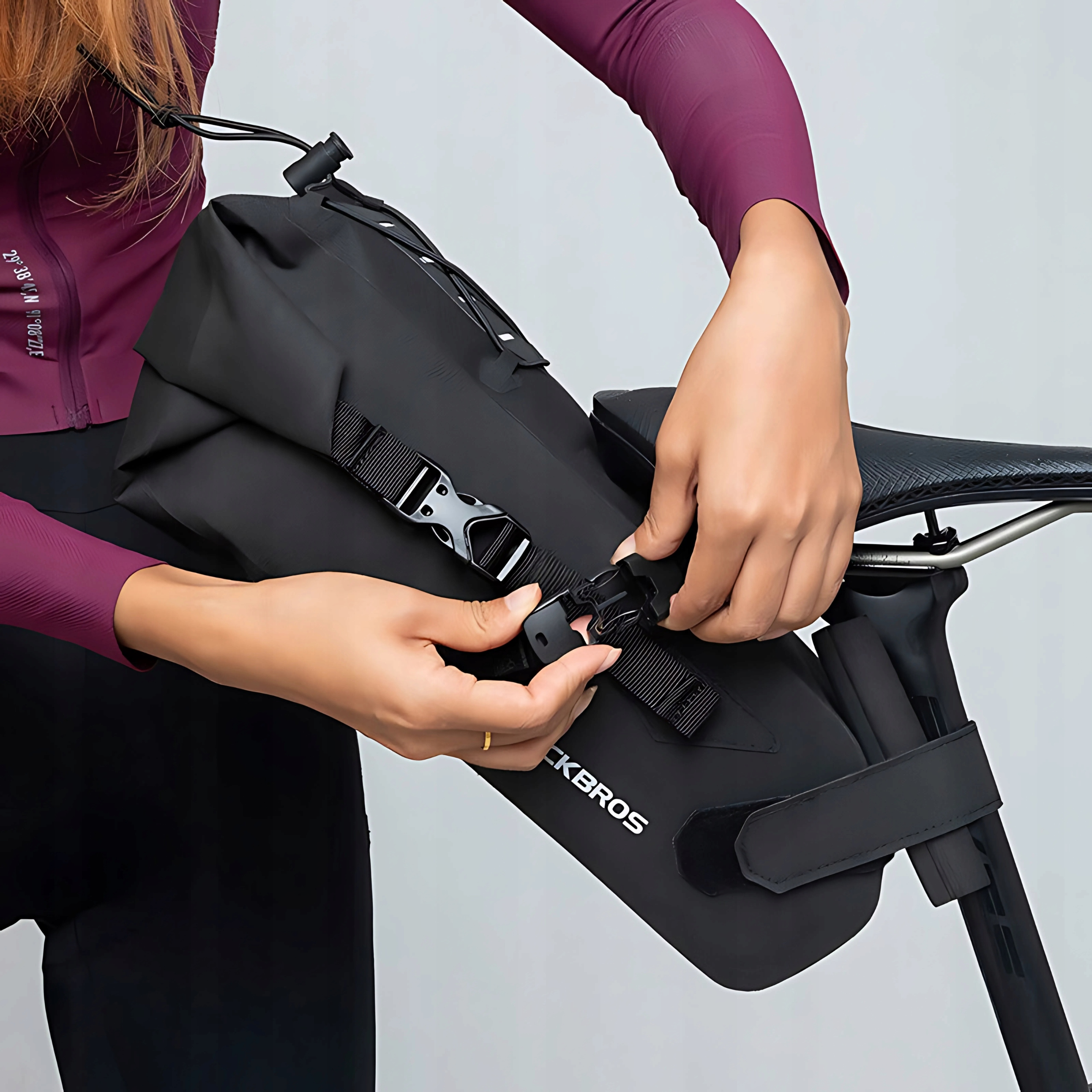 Osoba przypina czarną torbę Rockbros do siodełka rowerowego. Torba ma paski i klamry.