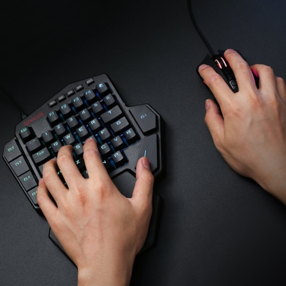 Le mani usano una tastiera da gioco su una superficie nera. I tasti sono illuminati.